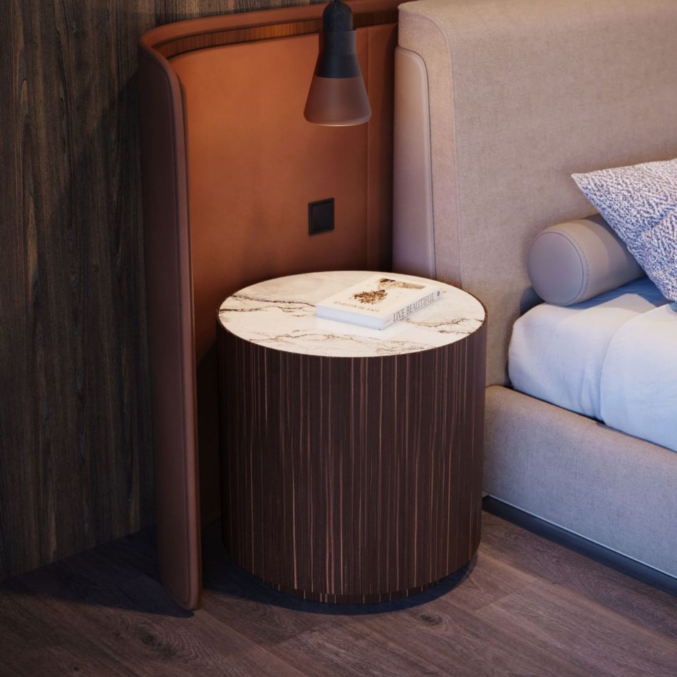The Drum Side Table appears beside a contemporary bed, its brown oak wood veneer and marble top adding sophistication to the warm bedroom ambiance. Styled with a book and illuminated by a pendant light, the table enhances the room’s serene atmosphere, fitting into luxury home furniture and modern bedroom furniture compositions.