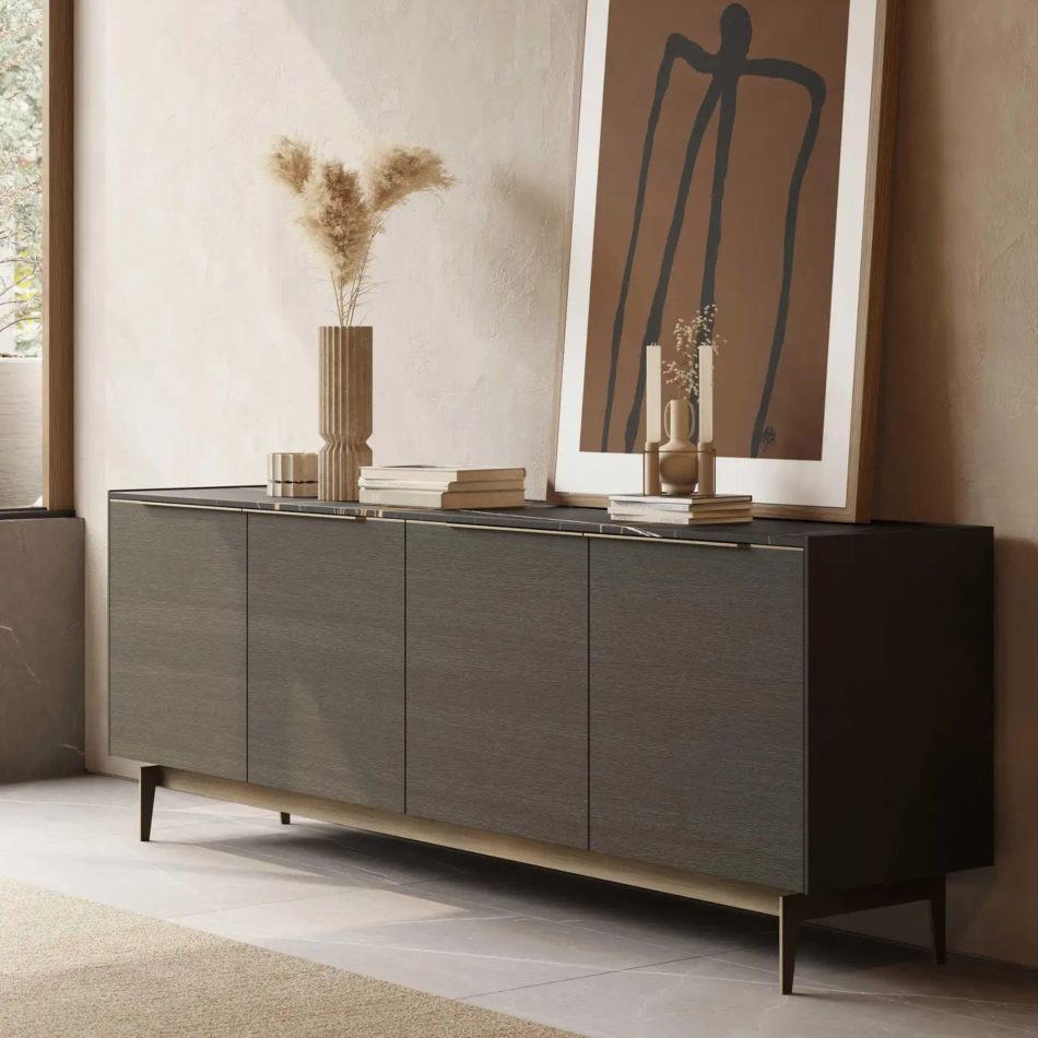 The Landform Sideboard brings structure to the room with its clean wood lines, styled with a ribbed vase of pampas, stacked books, and sculptural candleholders. A warm abstract artwork leans behind it, adding depth and contrast to the minimalist setting. The composition reflects casegoods furniture, balanced with the quiet elegance of luxury home furniture, and shaped to inspire subtle living room inspiration.