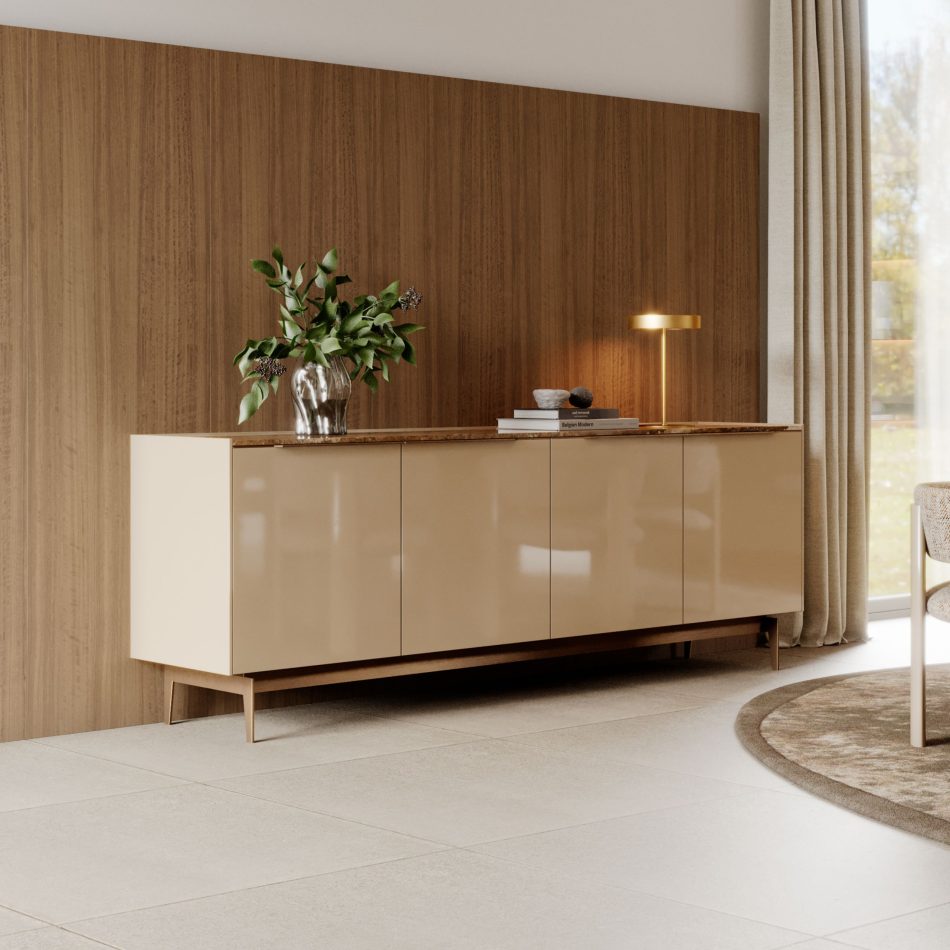A sleek beige sideboard stands against a wooden wall, decorated with a clear glass vase of green branches, a gold lamp, and a small stack of books. Soft curtains frame the window beside it, creating a serene, contemporary atmosphere. The vignette highlights curated home furniture, balanced with the simplicity of contemporary furniture, and shaped to inspire subtle dining room inspiration.