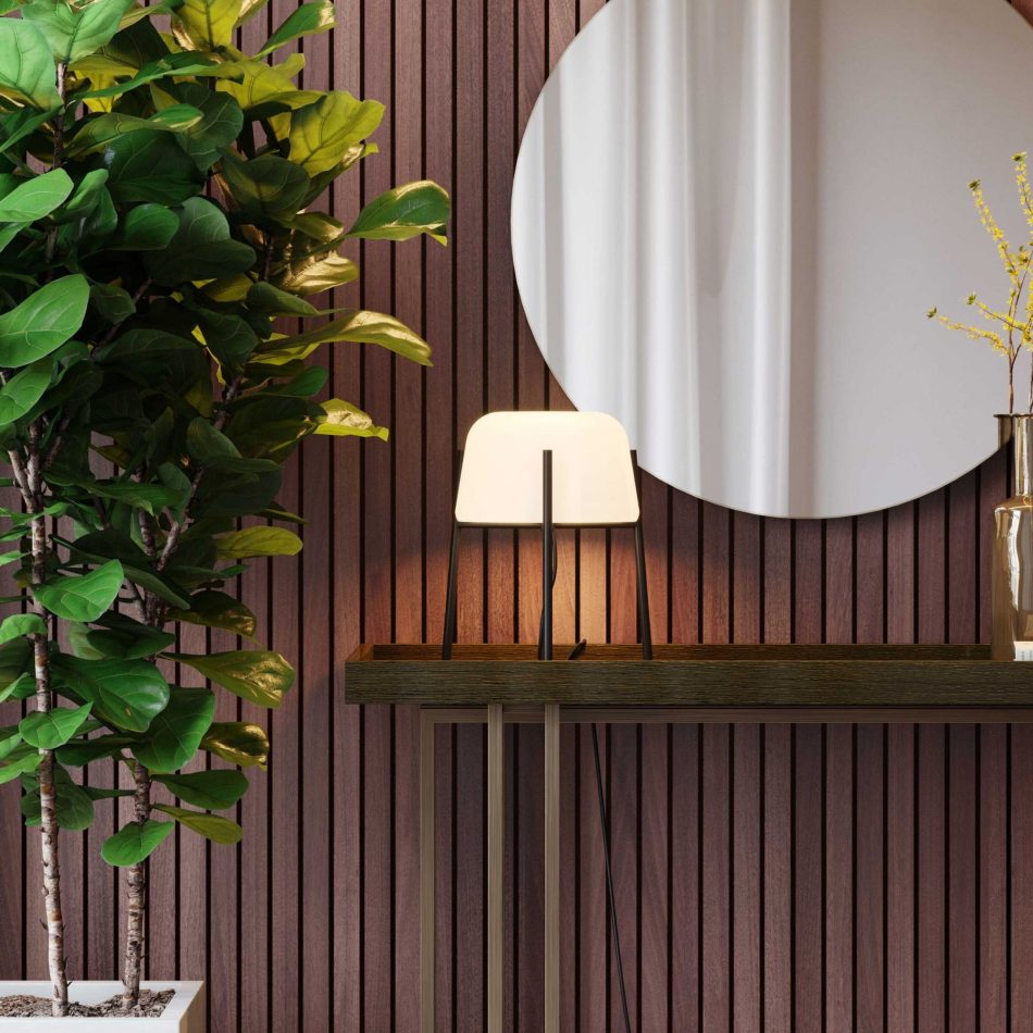 The wooden Vector console is styled with a dome‑shaped lamp, a brown glass vase, stacked books, and a lit candle, all set against vertical wooden paneling. The round mirror above reflects soft daylight and part of the room, while a potted plant adds a natural touch. The scene merges furniture luxury design and the warm simplicity of modern furniture.