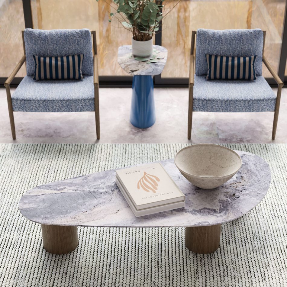 The Natur Coffee Table in a marbled finish anchors the seating area, its irregular top resting on wooden cylindrical legs. A ceramic bowl and art book add texture, while patterned armchairs and a marble side table frame the composition. The space blends elegant home furniture with sculptural design details and the clean balance of contemporary furniture.