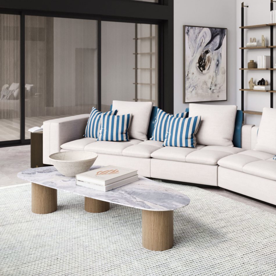 The Natur Coffee Table in light marble with wooden legs stands at the centre of a bright living room, styled with a decorative bowl and stacked books. A neutral sectional sofa, striped cushions, and a textured rug complete the serene setting, shaped by thoughtful living room design, elevated through elegant luxury home furniture, and complemented by furniture for living room.