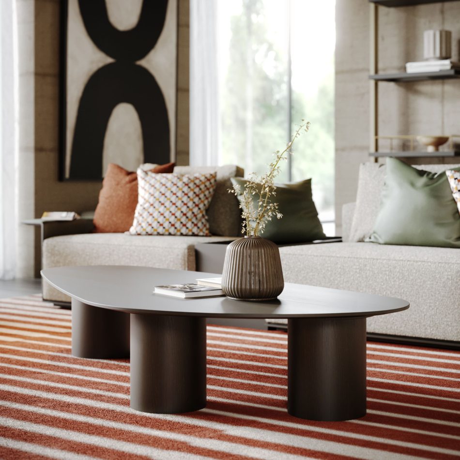The Natur Coffee Table in a smooth dark wood finish rests on a red‑and‑white striped rug, styled with a ceramic vase and books. A beige sofa with patterned cushions and a large abstract artwork complete the warm, modern setting. The composition highlights curated home furniture, softened by layered design details and shaped through thoughtful living room design.