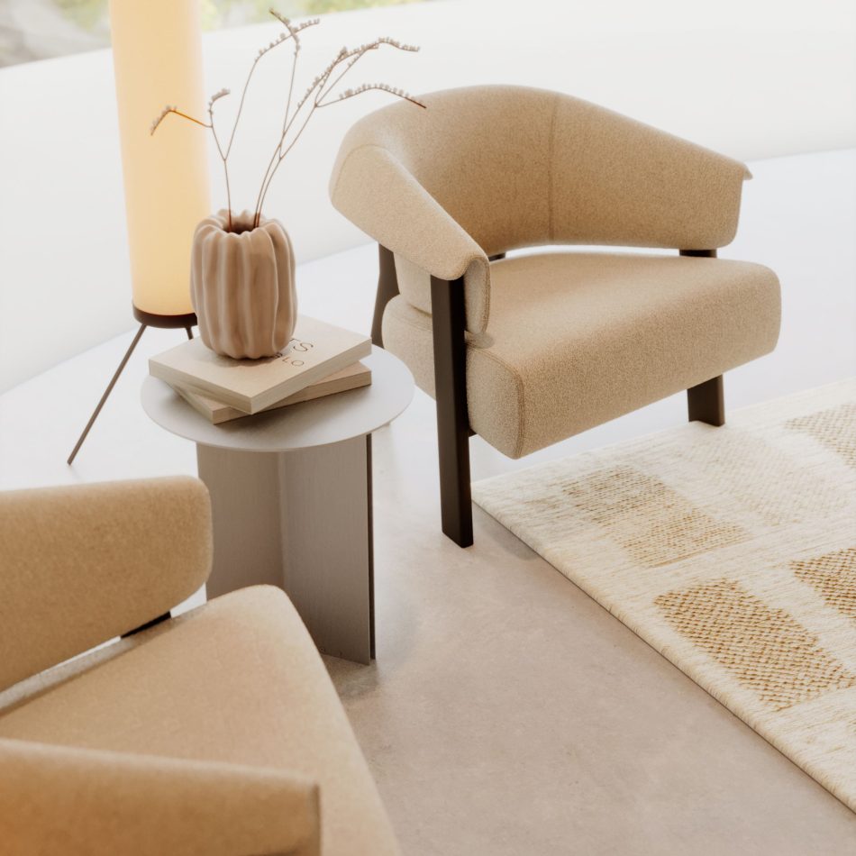 In a calm, minimalist seating area, the Steel Side Table in stainless steel brushed sits between two upholstered armchairs, its round top holding a vase and stacked books. Soft natural light and a warm floor lamp create a serene atmosphere that enhances the table’s quiet geometry. The space blends the clarity of modern furniture with the softness of living room inspiration, supported by subtle design details that elevate the room.