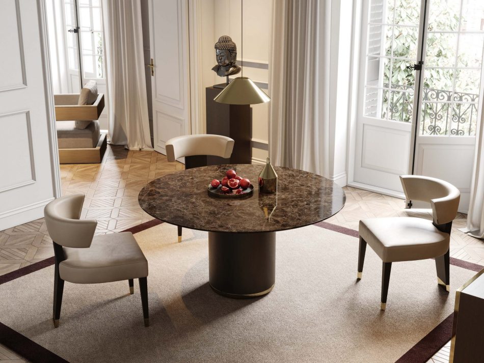 The Her Round Dining Table appears with a marble top surrounded by upholstered chairs, creating an intimate dining moment on a bordered rug. A bowl of pomegranates and a metallic vase form a sculptural centerpiece, complemented by a gold‑toned lamp and artistic accents on the sideboard. Natural light from the large windows enhances the harmony between formal dining room furniture, crafted modern furniture, and soft living room inspiration.