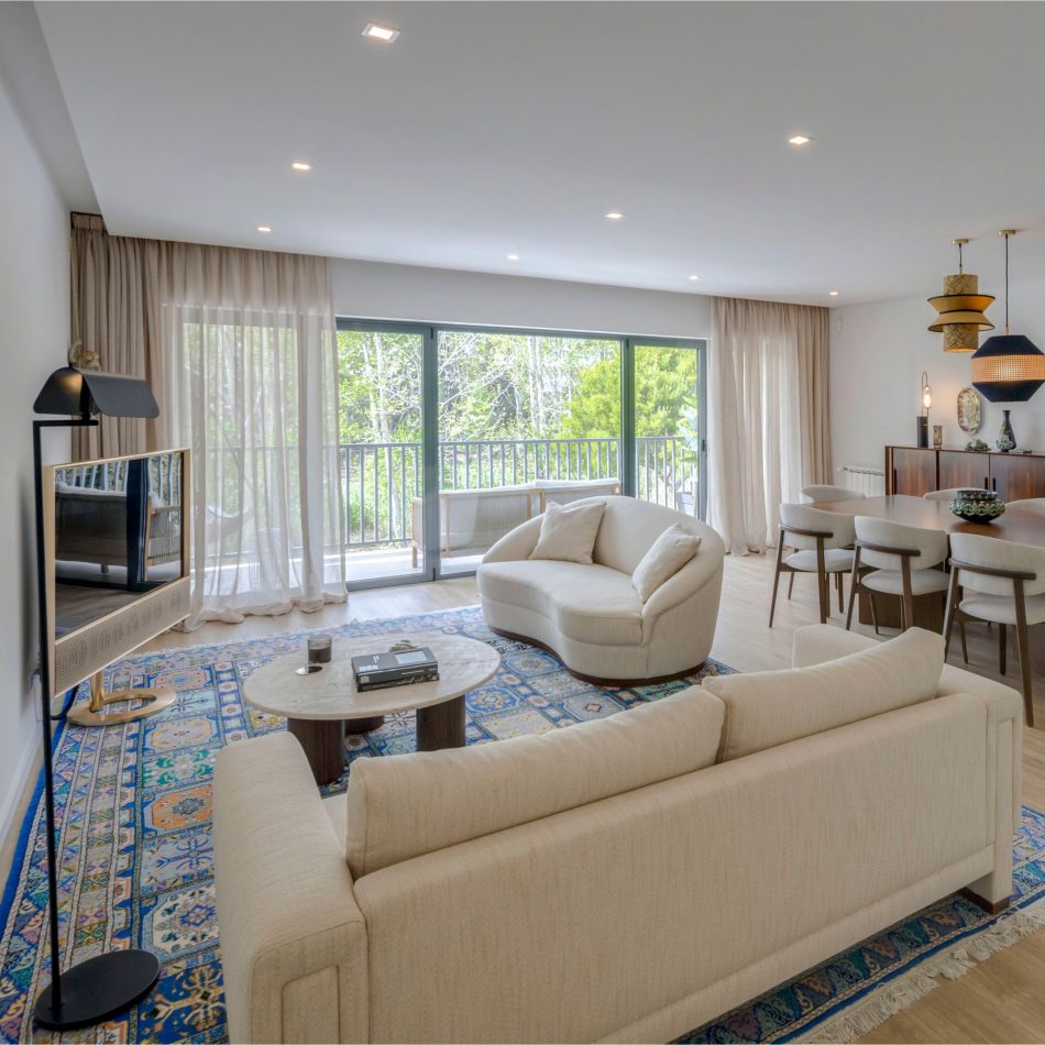 A bright open space where the Hillary Sofa brings soft, inviting comfort to the room. The Natur Coffee Table, with its travertine top, adds a natural contrast that complements the light-filled space. Subtle blue accents in the rug and lighting introduce calm and depth, shaping an atmosphere of modern design and quiet elegance.