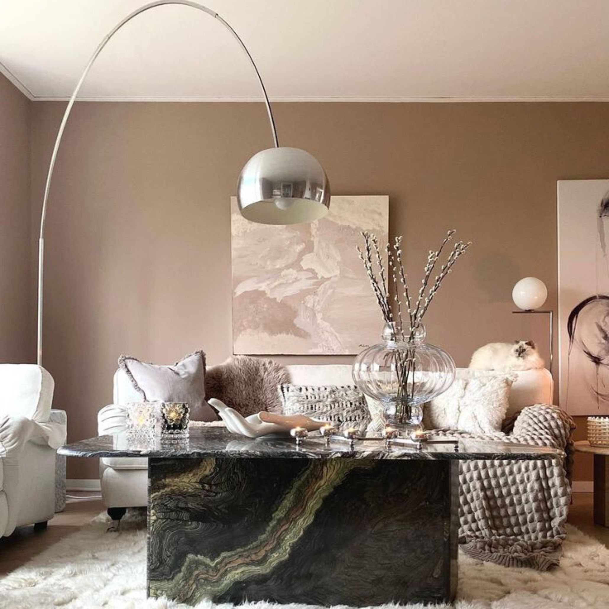 A stylish living room with soft textures and neutral tones, where the Arco Lamp arches over a dark stone coffee table.