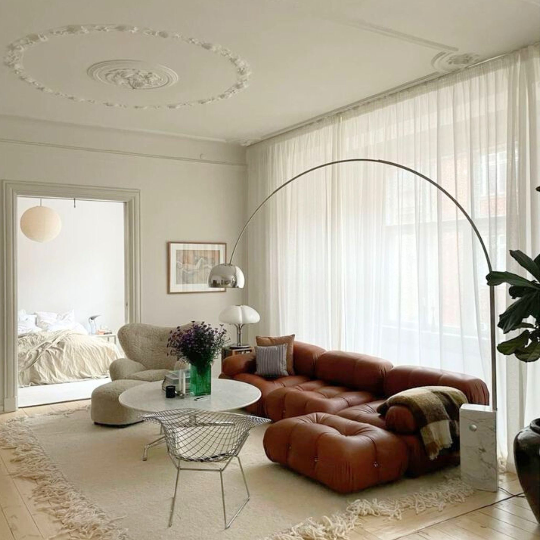 An elegant living room with an orange-toned modular sofa and white curtains, accented by the Arco Lamp’s graceful arch.