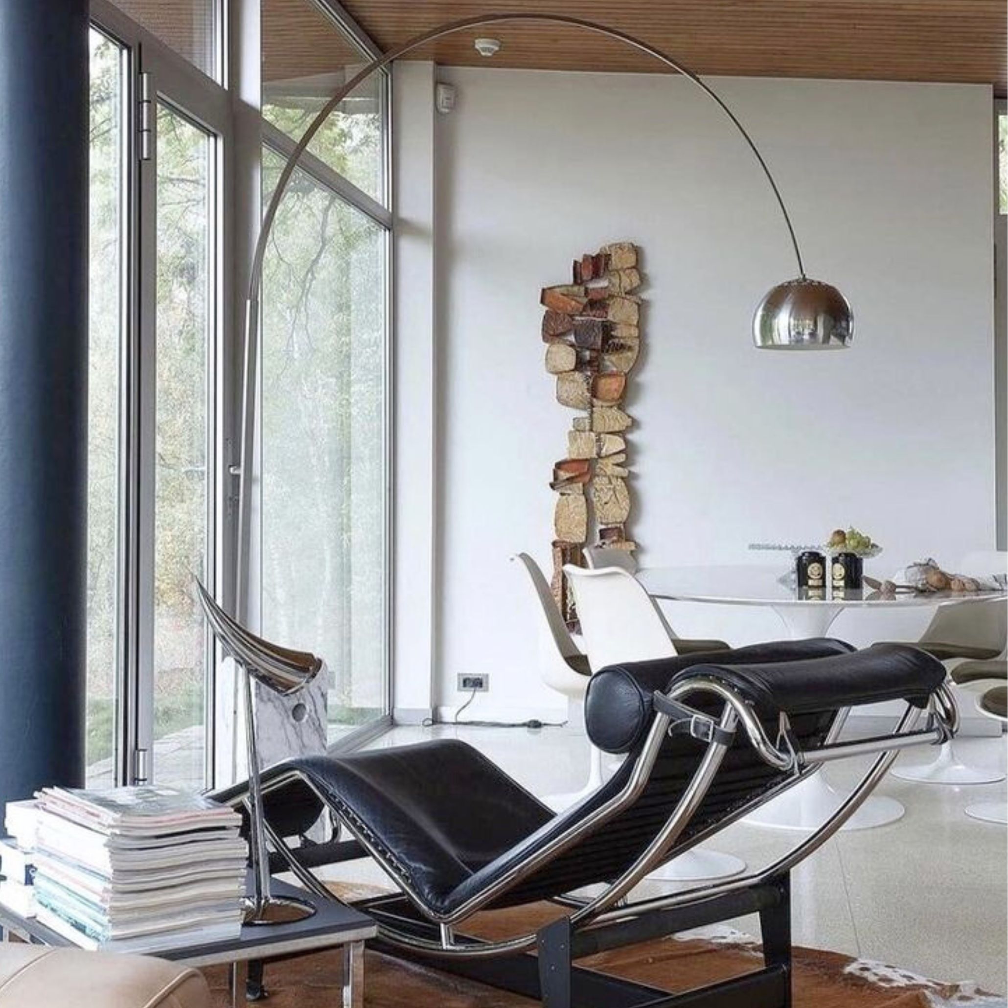 Modern reading nook with a black chaise lounge, floor-to-ceiling windows, and the Arco Lamp arching from behind.
