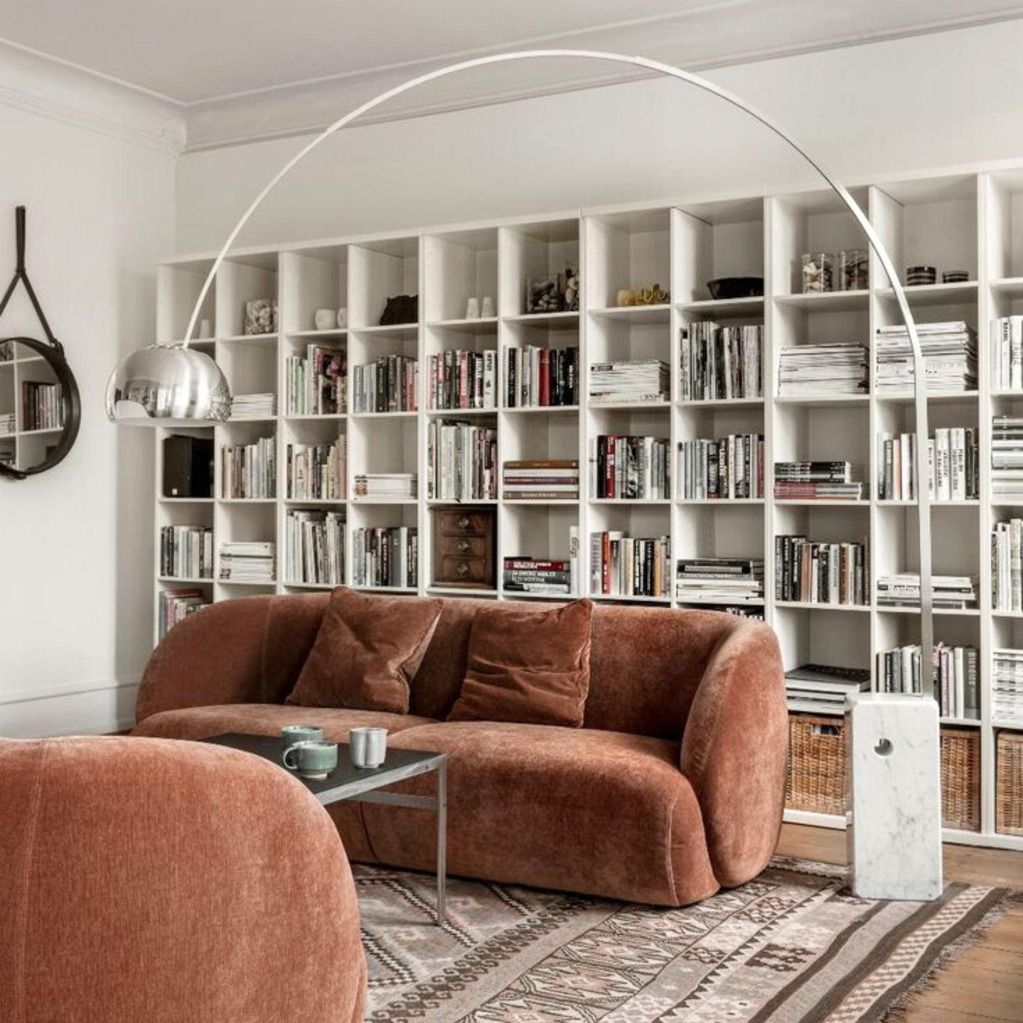 A cozy library-inspired space with a rust-colored velvet sofa and bookshelves, illuminated by the Arco Lamp.