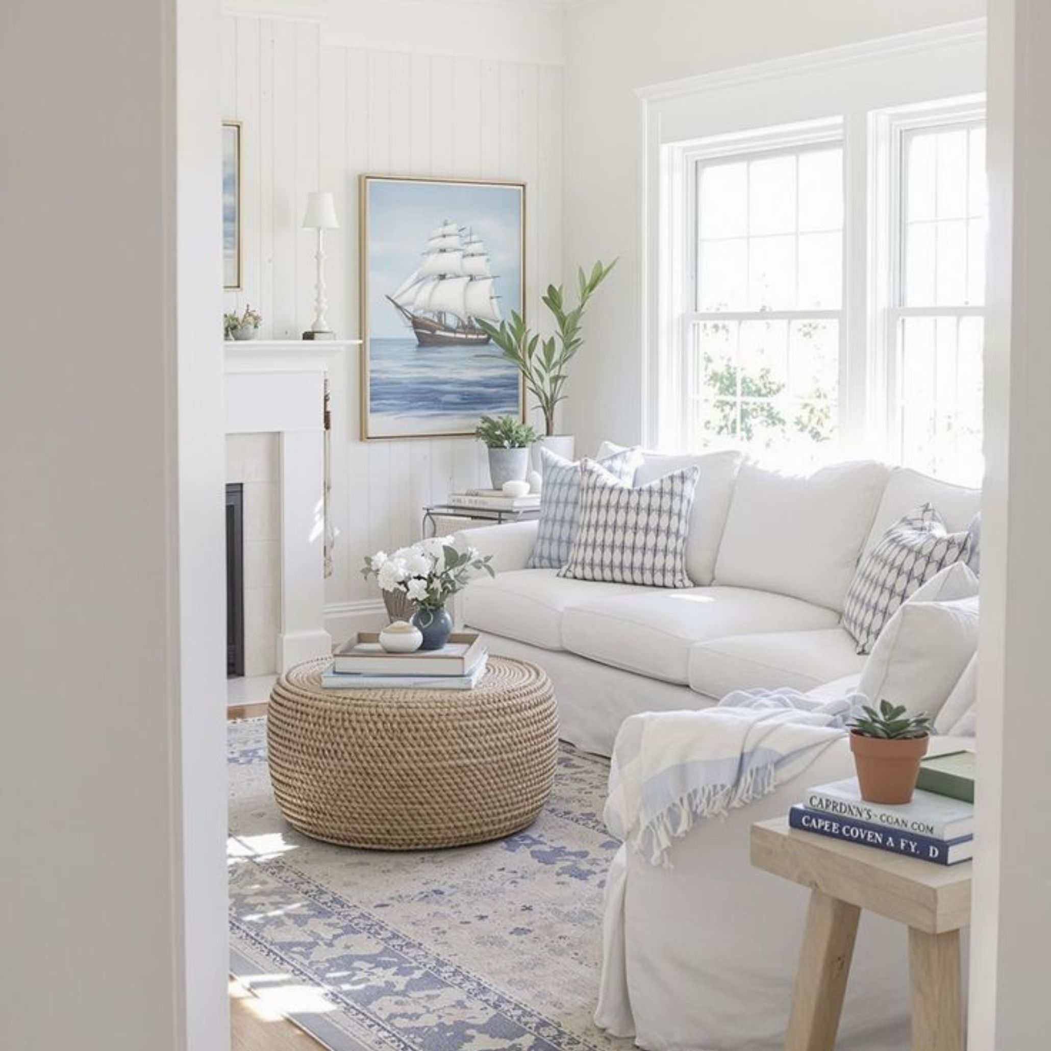 Bright coastal room with a white sofa, patterned pillows, nautical painting and natural textures that highlight the freshness and authenticity of Coastal Interior Design.