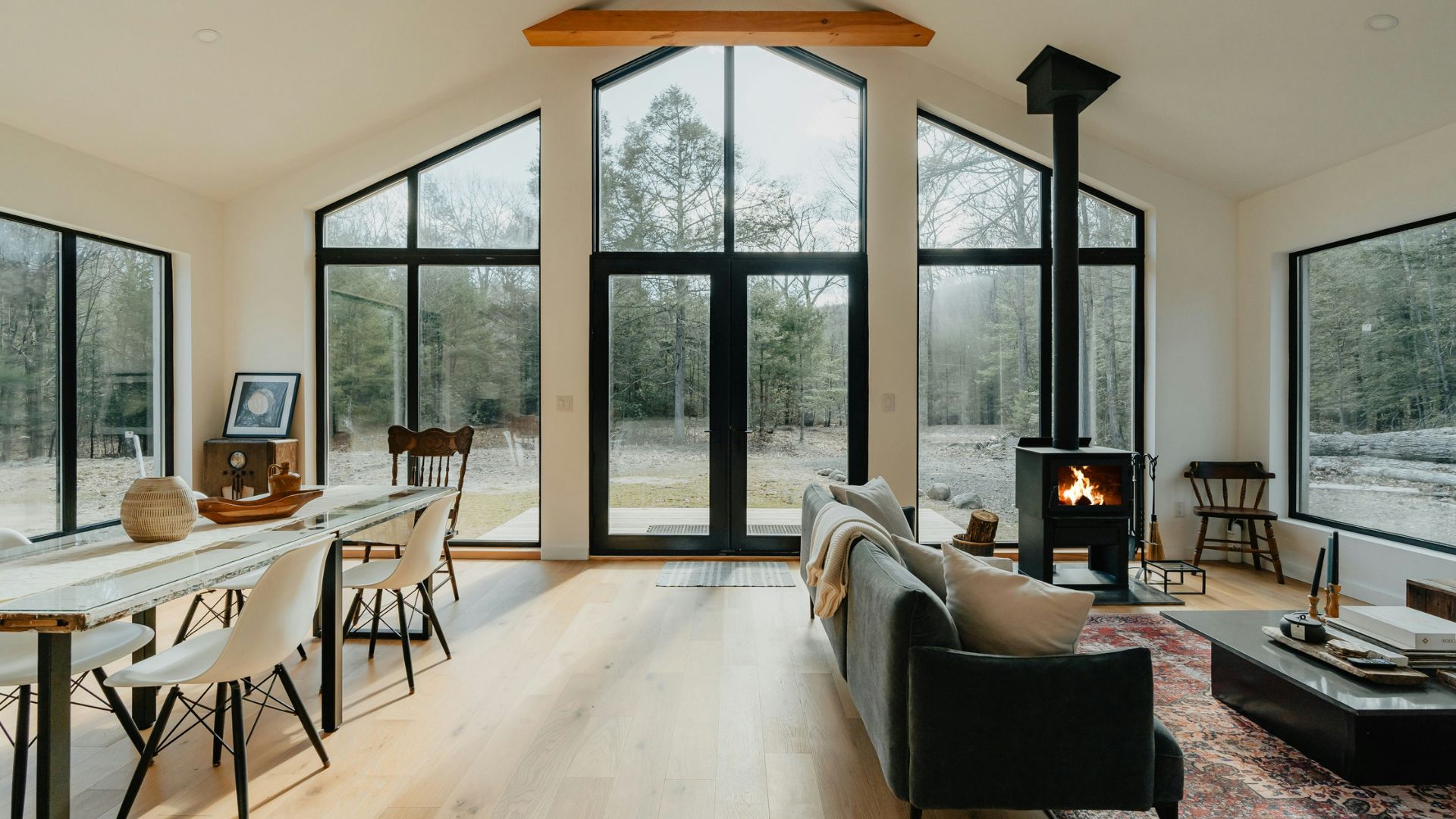 A modern cottagecore interior blending rustic elements with contemporary design. The open-plan space includes wood flooring, large windows letting in abundant natural light, a sleek fireplace, and minimalist furniture, illustrating how the style embraces modern luxury.
