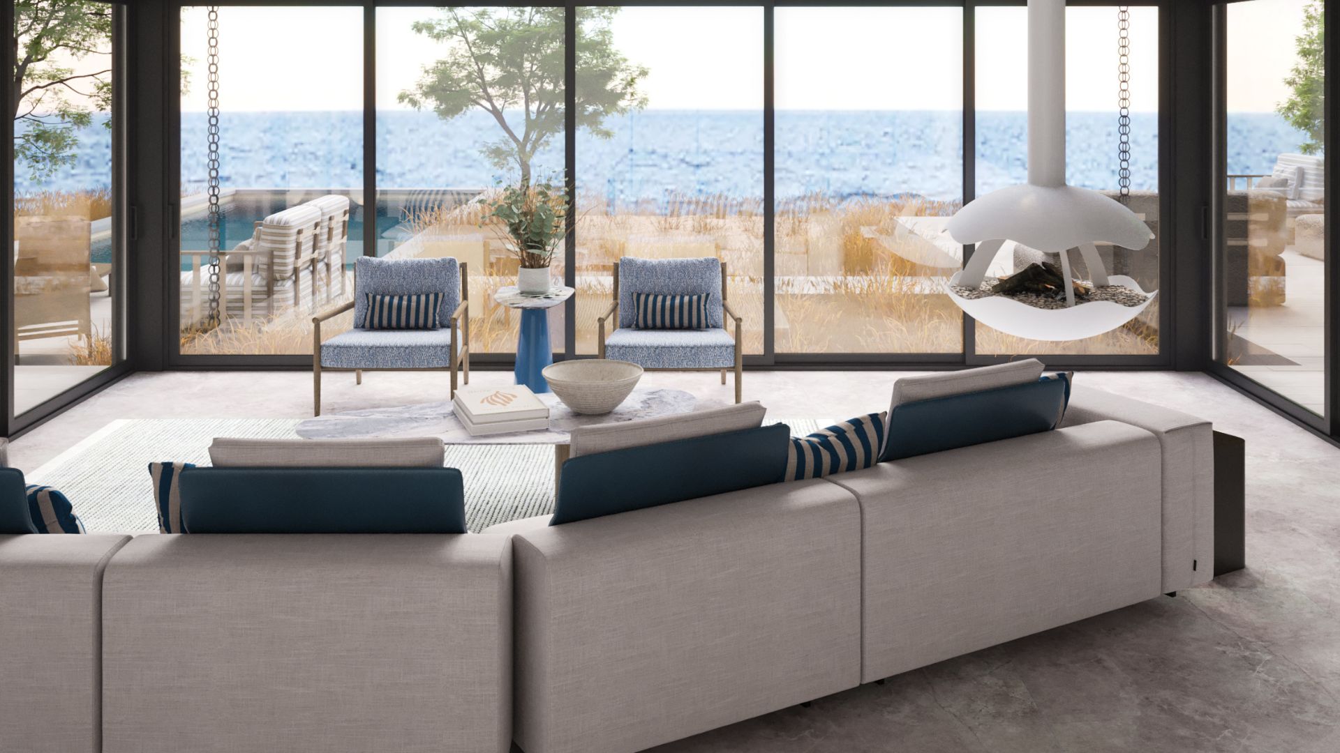 A serene and elegant Hamptons Style House living room featuring the Margem Sofa in neutral tones with soft blue accent pillows, paired with two Landform Armchairs in blue textured upholstery. The airy interior, with a view to the sea, reflects a sophisticated balance of comfort and modern furniture within a Beach House Hamptons Style setting.