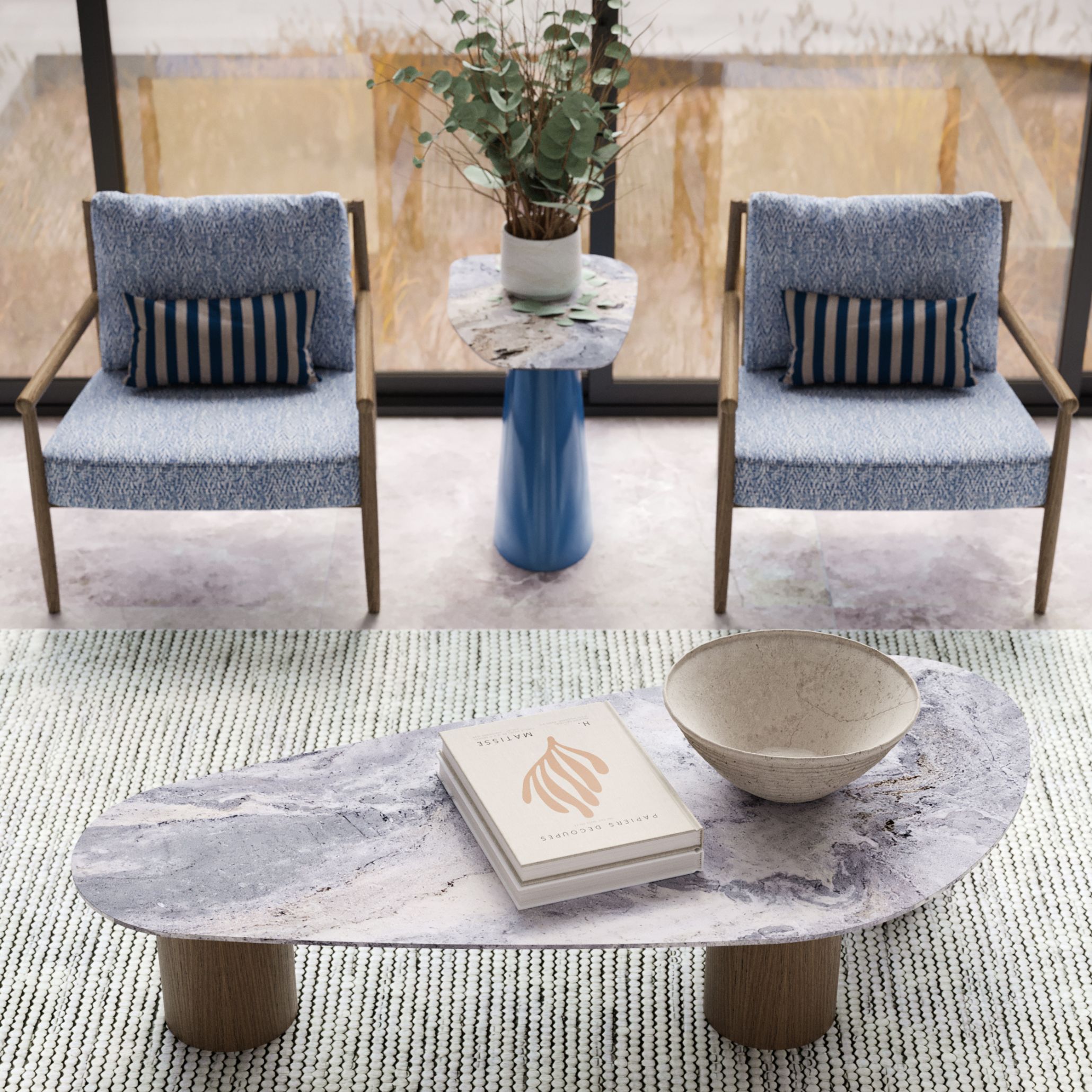 A refined Hamptons Style lounge corner featuring the Natur Coffee Table with wooden bases and River Blue marble top, two Landform Armchairs in textured blue upholstery, and the sculptural Stone Side Table with a high-gloss blue base and River Blue marble top. This ensemble embodies modern table design and sophisticated seaside living.
