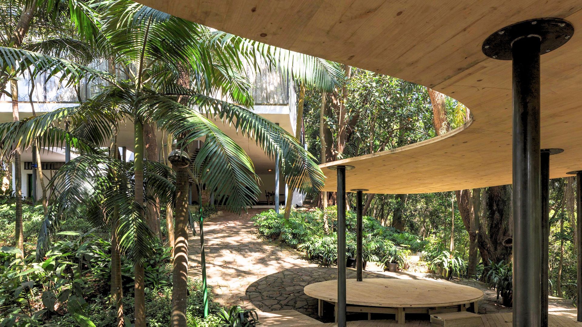View of the Casa de Vidro by Lina Bo Bardi showcasing its organic roof structure blending seamlessly with lush greenery. This example of Lina Bo Bardi architecture reflects her integration of nature with contemporary architecture, emphasizing transparency and coexistence with the environment.