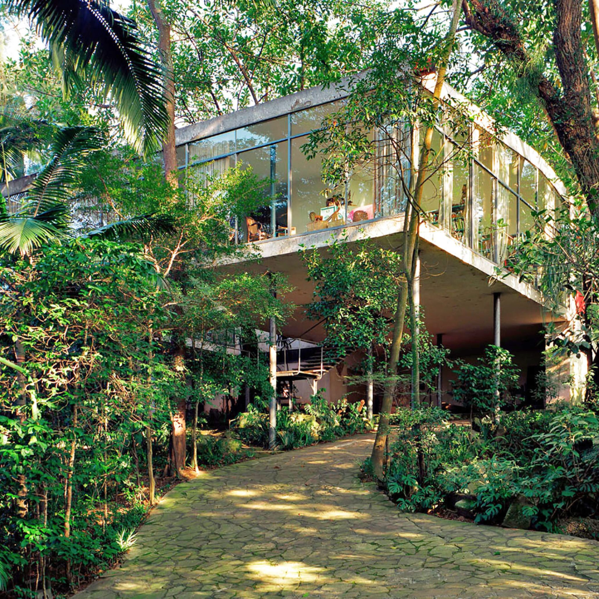 Main view of the Casa de Vidro by Lina Bo Bardi, with its elevated glass structure resting on slender columns. This landmark of contemporary architecture illustrates Bo Bardi’s philosophy of integrating living spaces into the natural landscape with structural lightness and transparency.