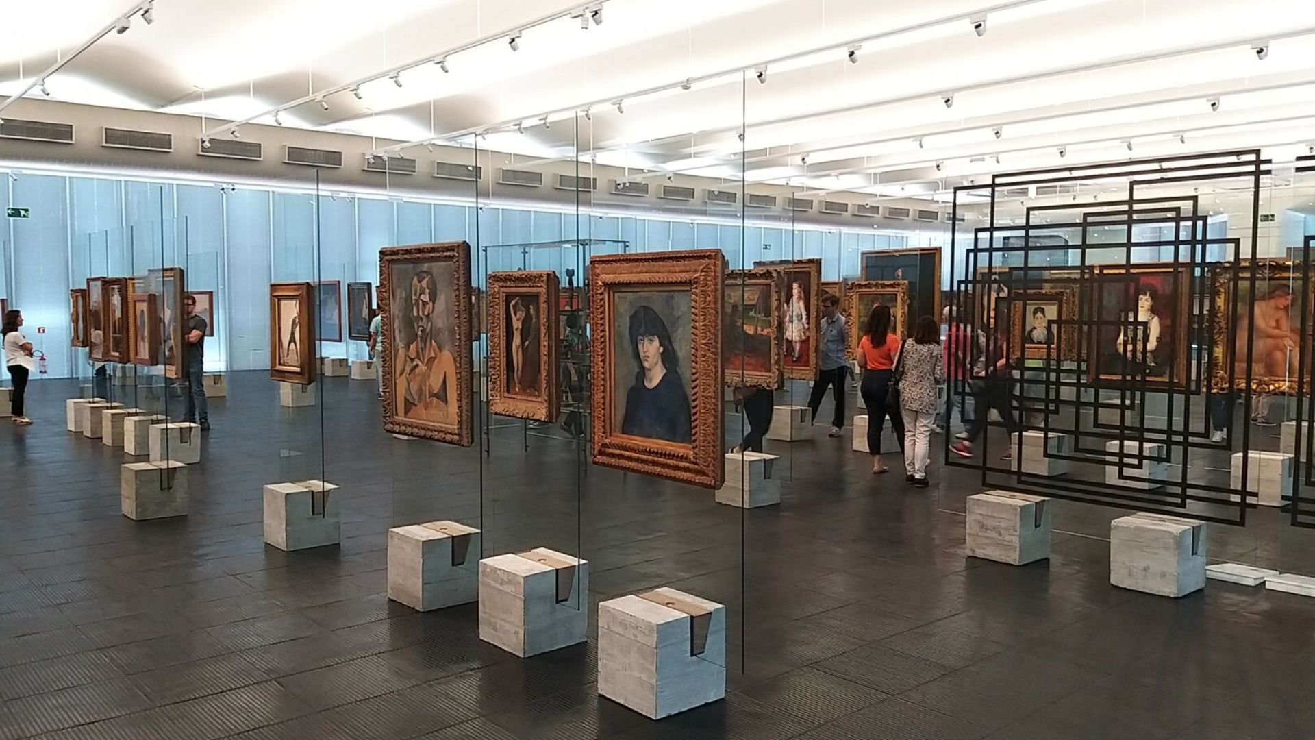 The iconic Glass Easels designed by Lina Bo Bardi inside MASP. Thick glass panels mounted on concrete bases display artworks with transparency, exemplifying her groundbreaking approach to exhibition design and her philosophy of cultural accessibility.