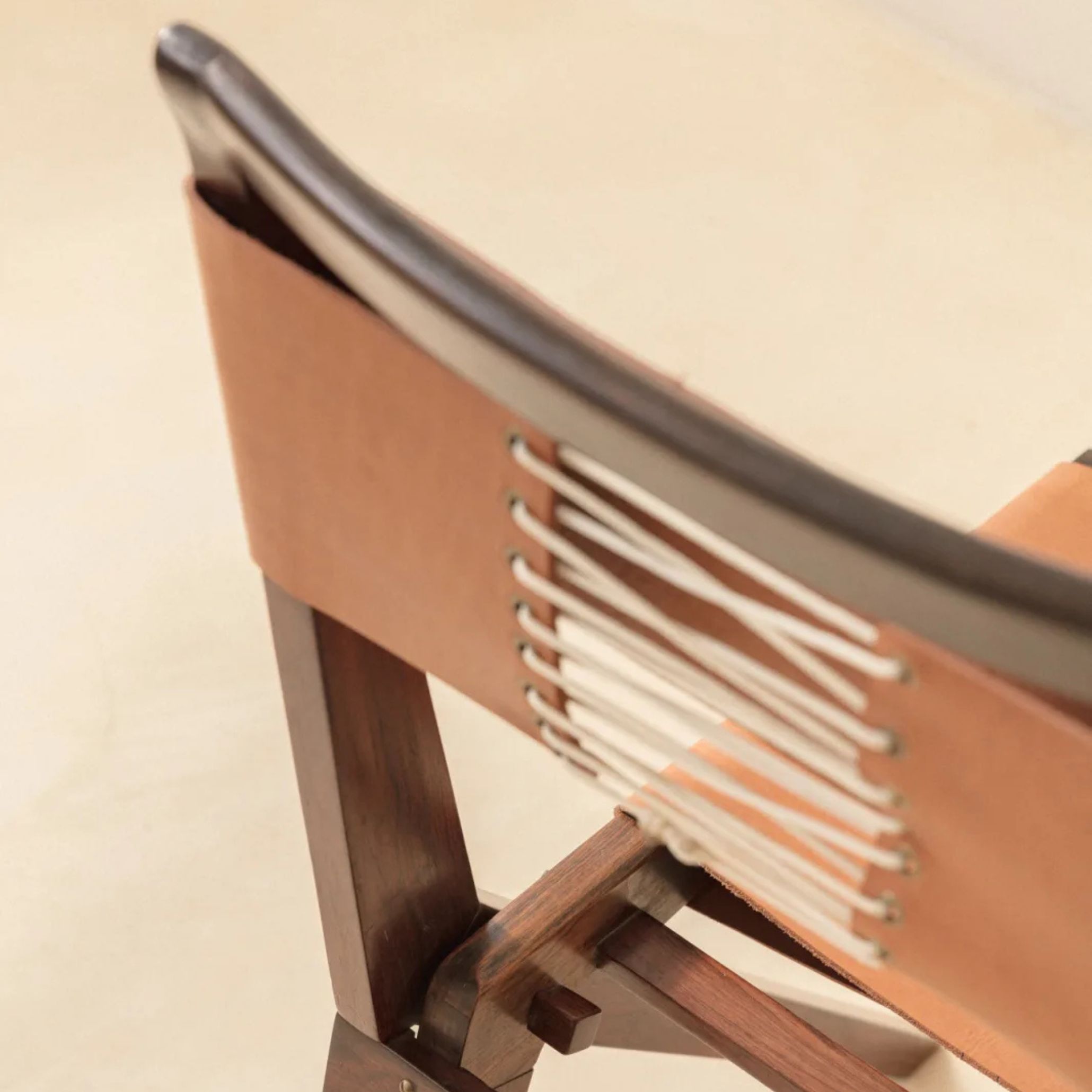 Close-up image of a MASP Chair by Lina Bo Bardi, highlighting the wooden structure, camel leather seat, and backrest with cross-laced detailing. This detail showcases her meticulous attention to craftsmanship and purpose in furniture design within the broader context of Lina Bo Bardi architecture.