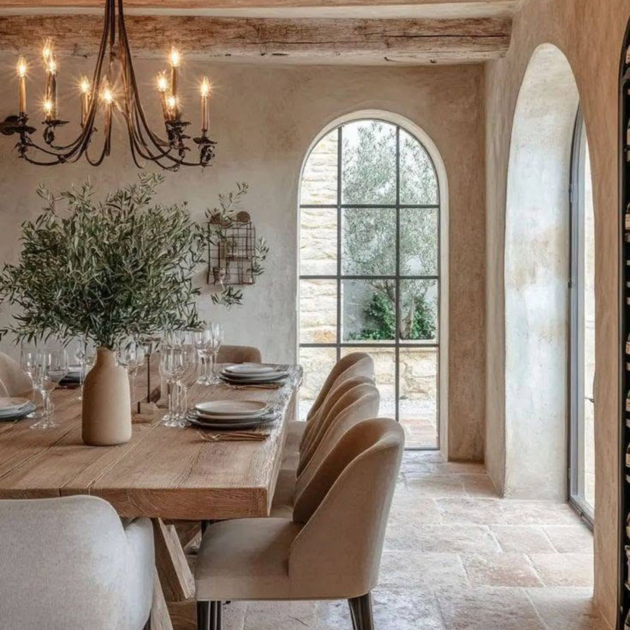 A richly textured Tuscan dining room filled with rustic charm, showcasing plastered walls in soft beige, aged wooden beams, and a robust iron chandelier hanging above a handcrafted wood table. This cozy and intimate setting emphasizes the value of craftsmanship and tradition in Tuscan interior design.
