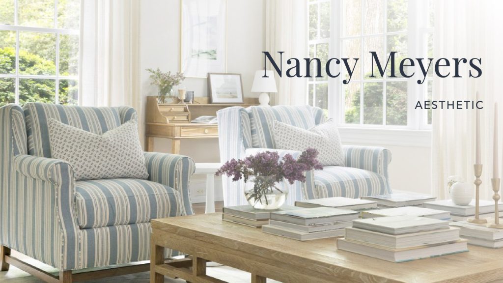 Cozy and elegant living room inspired by the Nancy Meyers aesthetic, featuring two striped armchairs with patterned cushions, a wooden coffee table stacked with books, fresh lilac flowers in a glass vase, and large windows flooding the room with natural light.