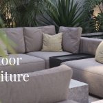 A cozy and elegant outdoor lounge setting featuring a beige modular sofa with textured cushions in earthy tones of yellow and moss green, surrounded by tropical plants and soft lighting. The image serves as a visual banner for “Outdoor Furniture Trends 2025”, capturing the essence of refined textures, layered comfort, and nature-inspired colour palettes that define the year’s outdoor design direction.