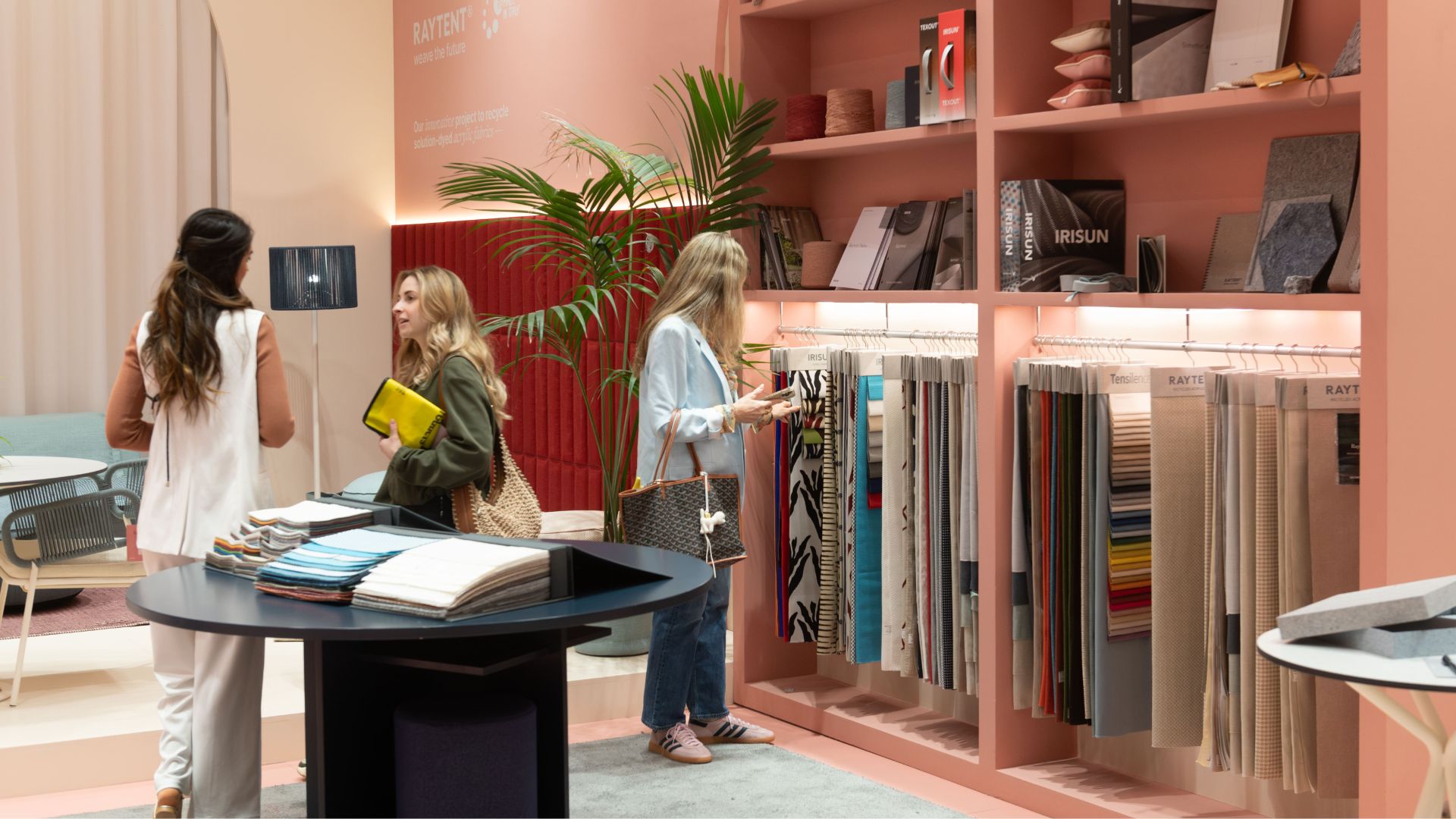 Visitors explore an exhibition at iSaloni 2025, surrounded by fabric samples, material displays, and engaging in conversations about interior design and furniture trends.