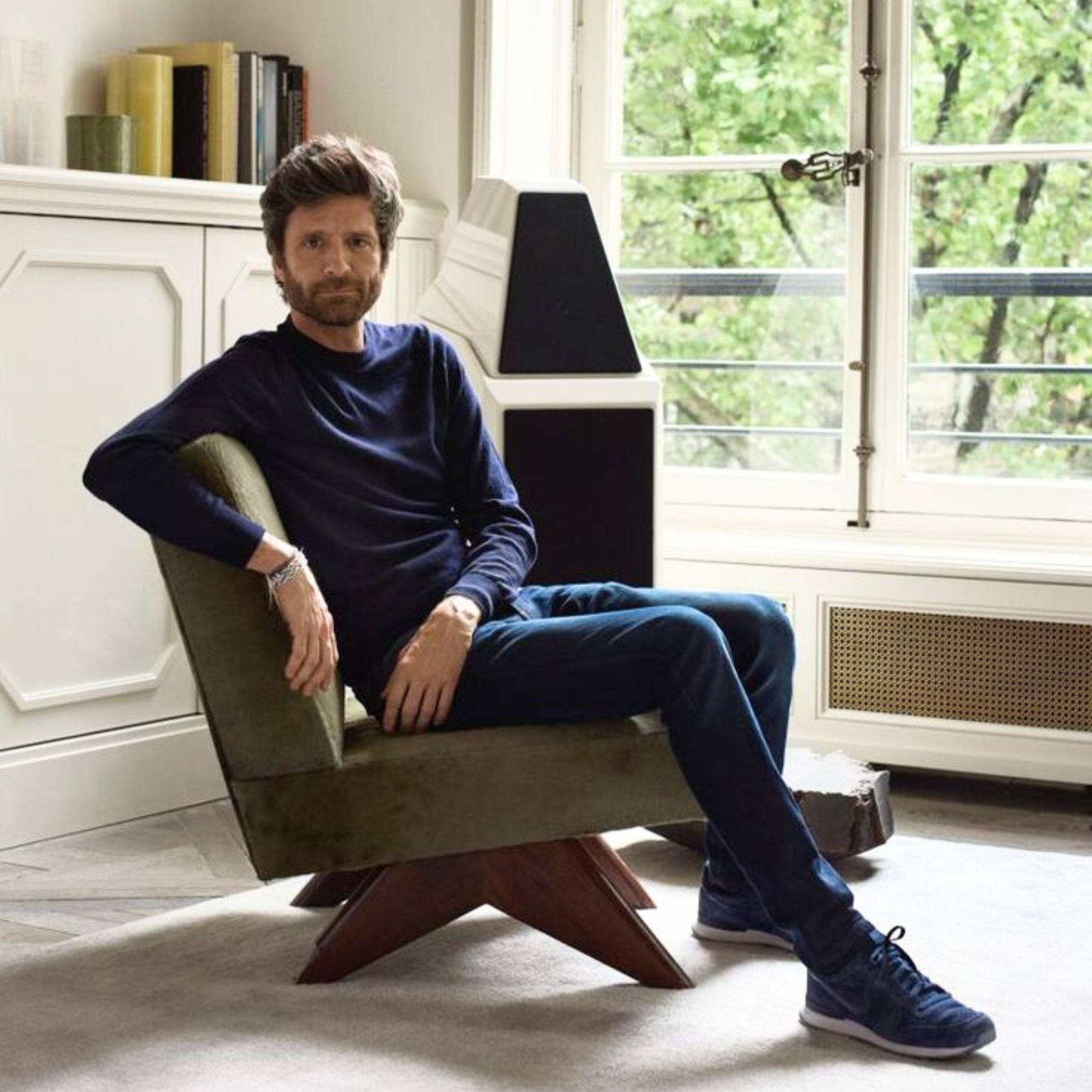 Joseph Dirand seated in a minimalist interior, surrounded by natural light and sculptural furnishings. The scene reflects his precise way of shaping space, where proportion, texture, and alignment evolve together into a coherent architectural composition.