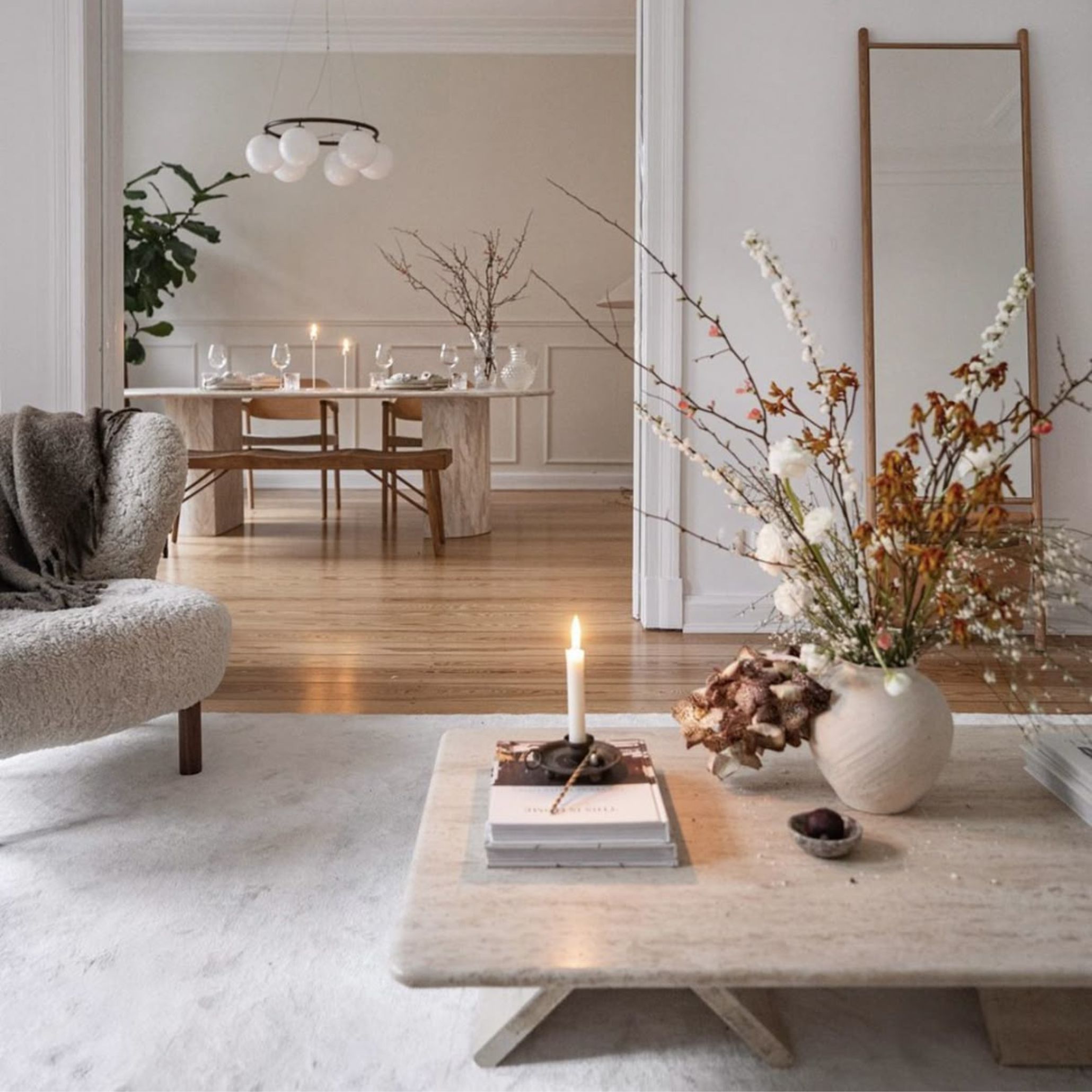 Scandinavian-style living and dining area with pale walls, layered lighting, and reflective surfaces to enhance natural light during Nordic winters.