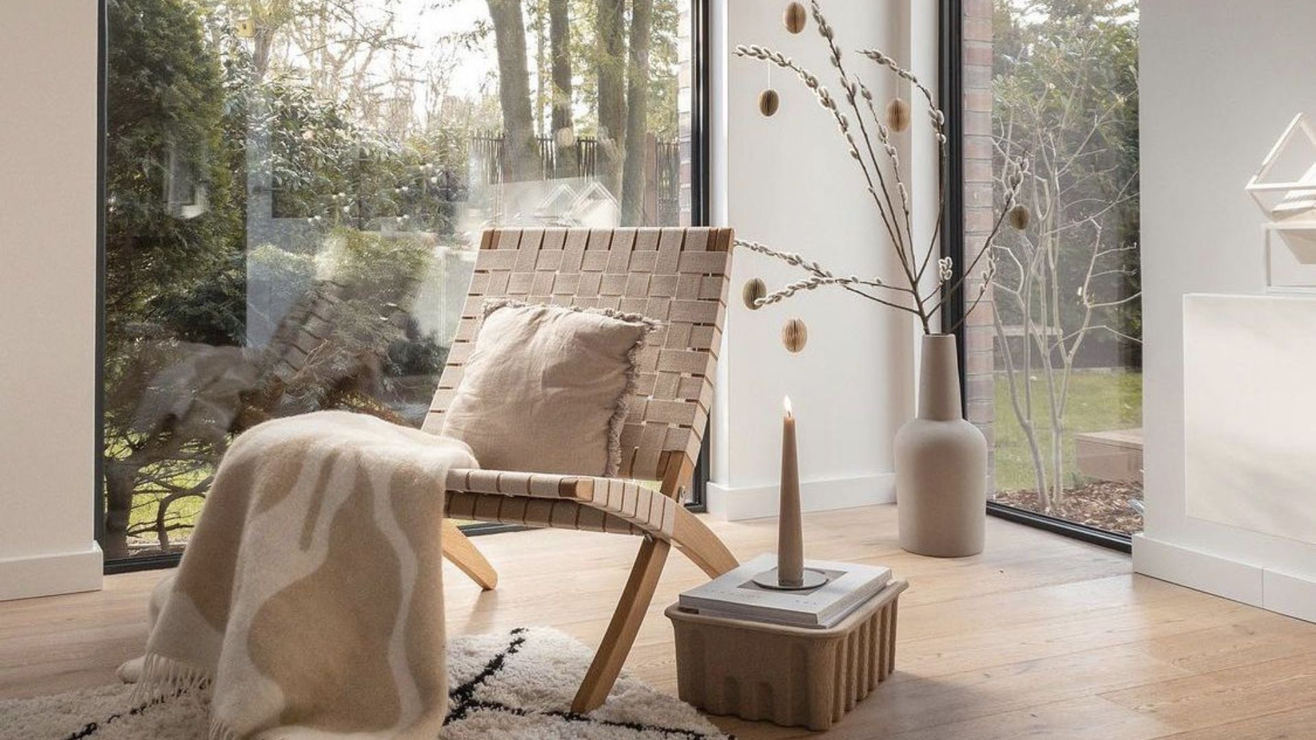 Scandinavian winter nook with woven lounge chair, wool throw, candlelight, and natural textures creating hygge comfort.