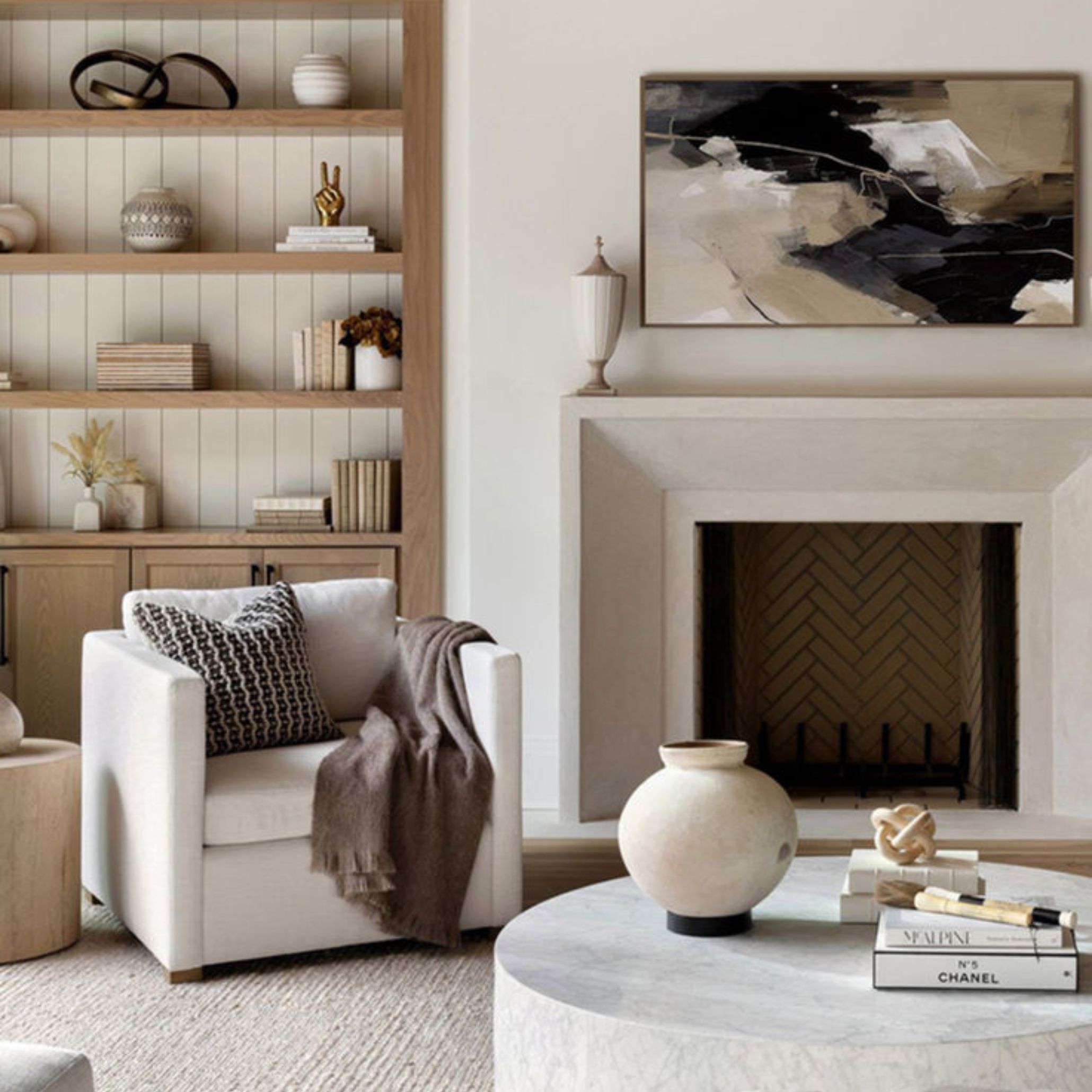 Transitional Style reading corner featuring a white armchair with a patterned cushion, round marble coffee table with decorative objects, built-in wooden bookshelf, and a minimalist fireplace with abstract artwork - showcasing a harmonious blend of traditional warmth and contemporary clarity.