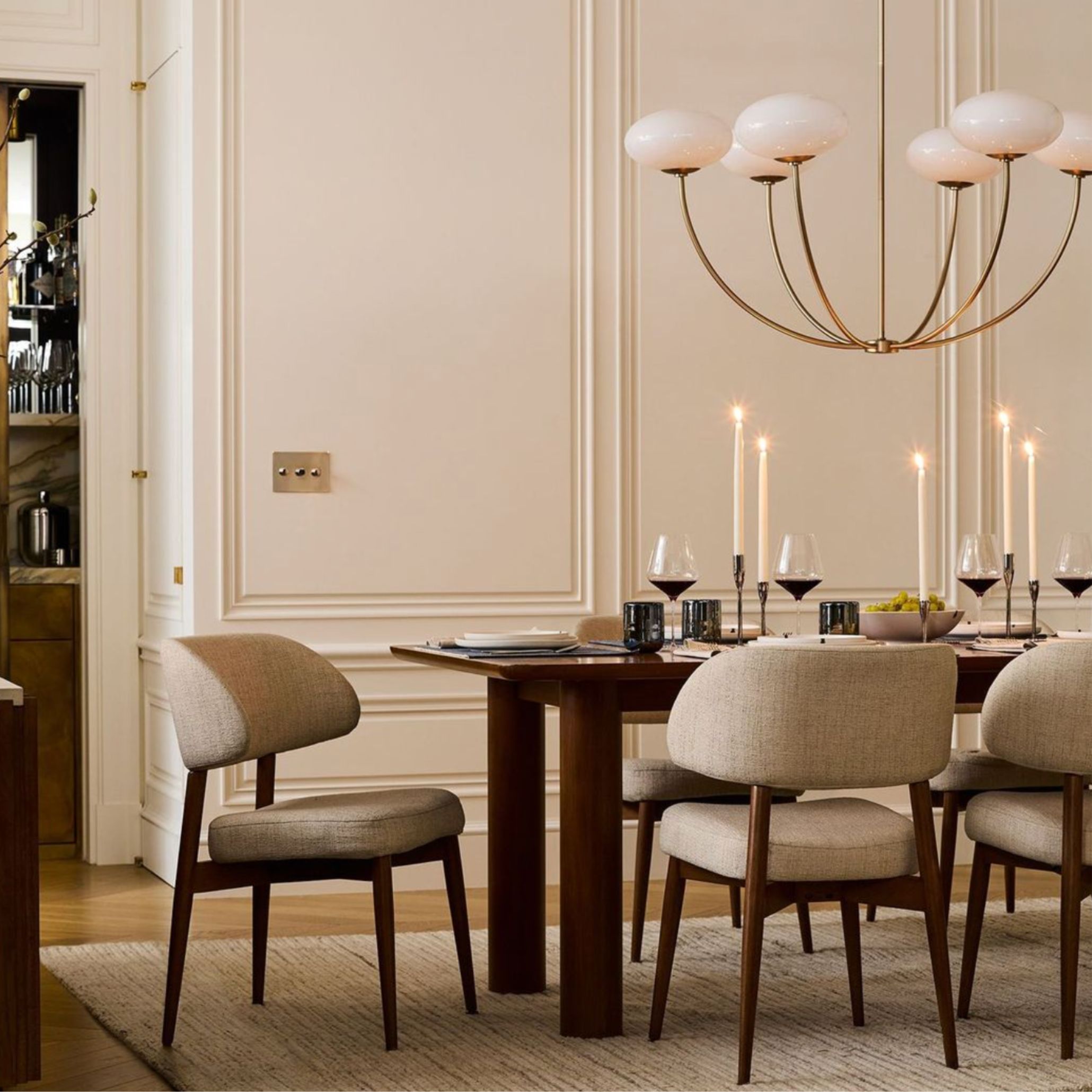 Refined dining room with sculptural chandelier, soft candlelight, and curated tableware. The layered lighting and intentional accessories - from wine glasses to ceramic accents - create warmth and understated elegance, embodying the quiet transformation of Transitional Design.