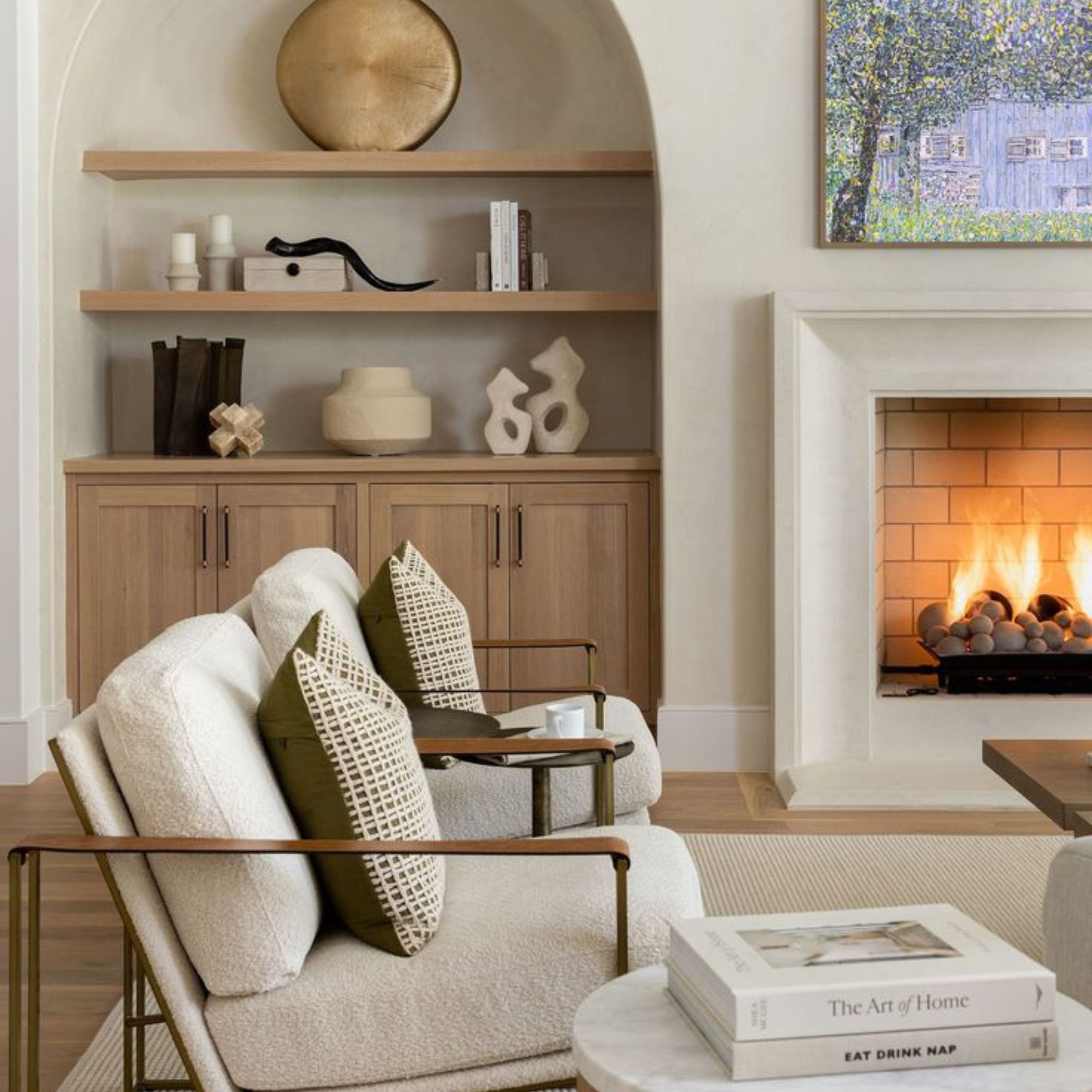 Cozy living room featuring plush armchairs, a marble side table, and a built-in cabinet with sculptural accessories. Soft illumination and thoughtfully placed objects - books, ceramics, and artwork - reflect the restraint and warmth central to Transitional Interior Design.