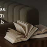 Stylish interior with a textured green sofa and scalloped-edge wooden coffee table displaying open books, evoking a cozy, intellectual ambiance. Overlay text reads 'Interior Design Trends for 2026,' suggesting a focus on upcoming home decor inspirations.