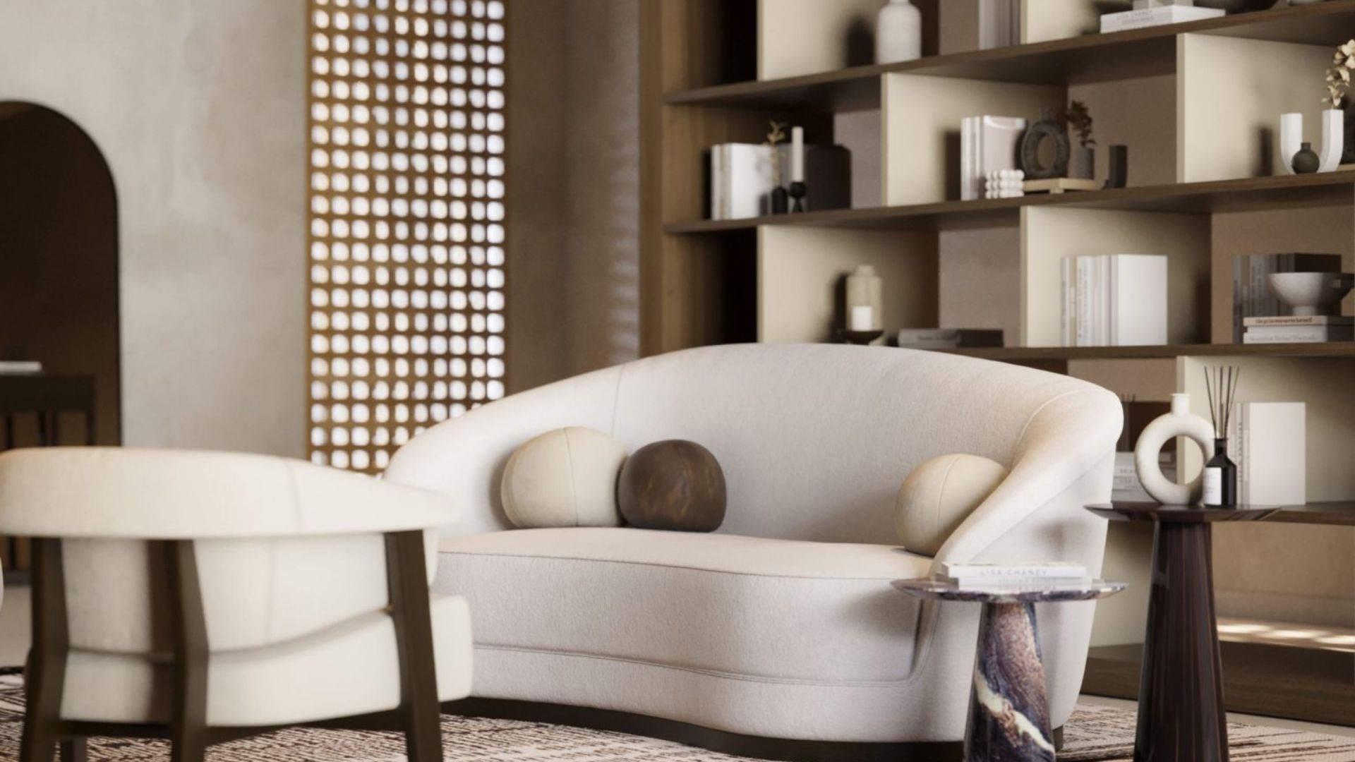 Elegant living room featuring the Hillary Sofa - a curved, upholstered loveseat with round accent pillows - paired with a matching armchair and sculptural side tables. The built-in shelving and perforated screen add texture and depth, reflecting the 2026 trend of transitional sofas as playful, stylish design statements.