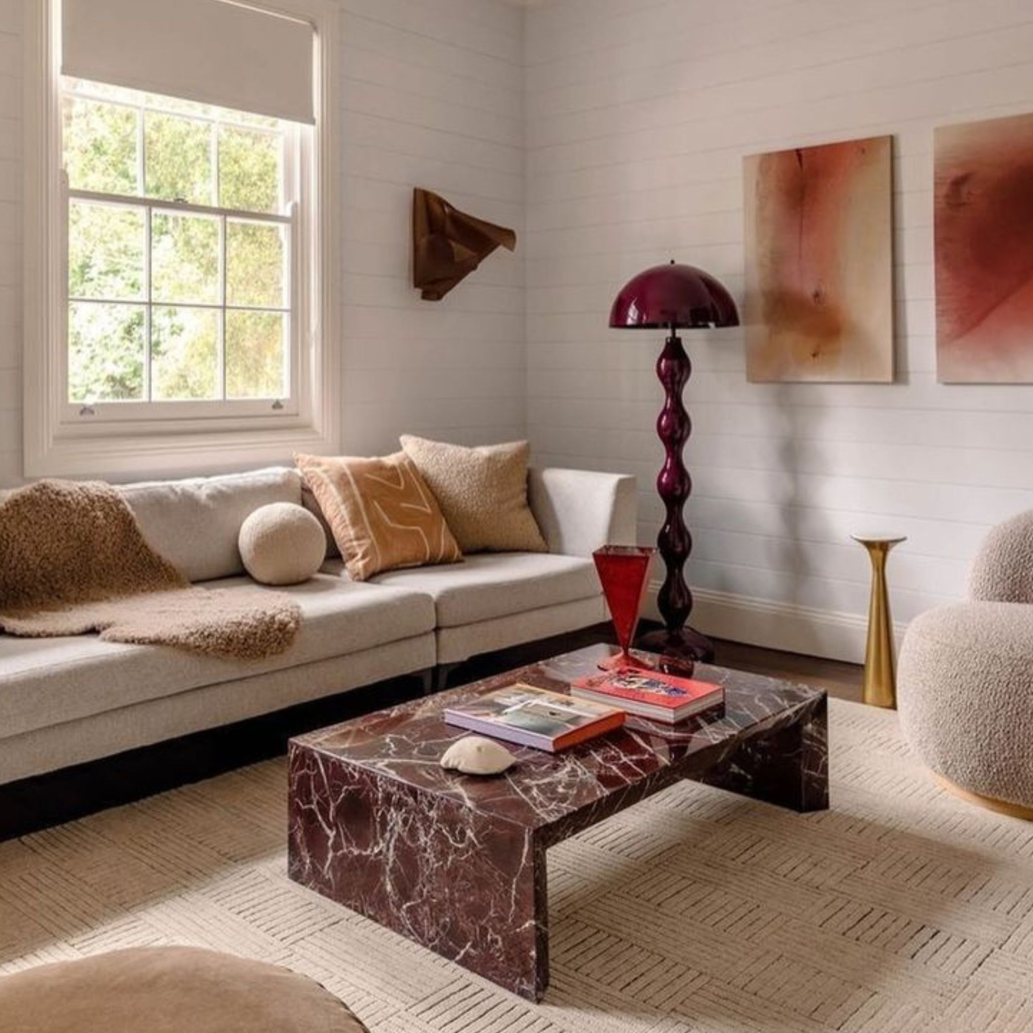 A cozy living room featuring a light sectional sofa, textured pillows, and a Rosso Leavanto marble coffee table. Sculptural lighting and abstract art add warmth and personality, showcasing how Rosso Levanto and other expressive materials define the layered aesthetic of 2026.