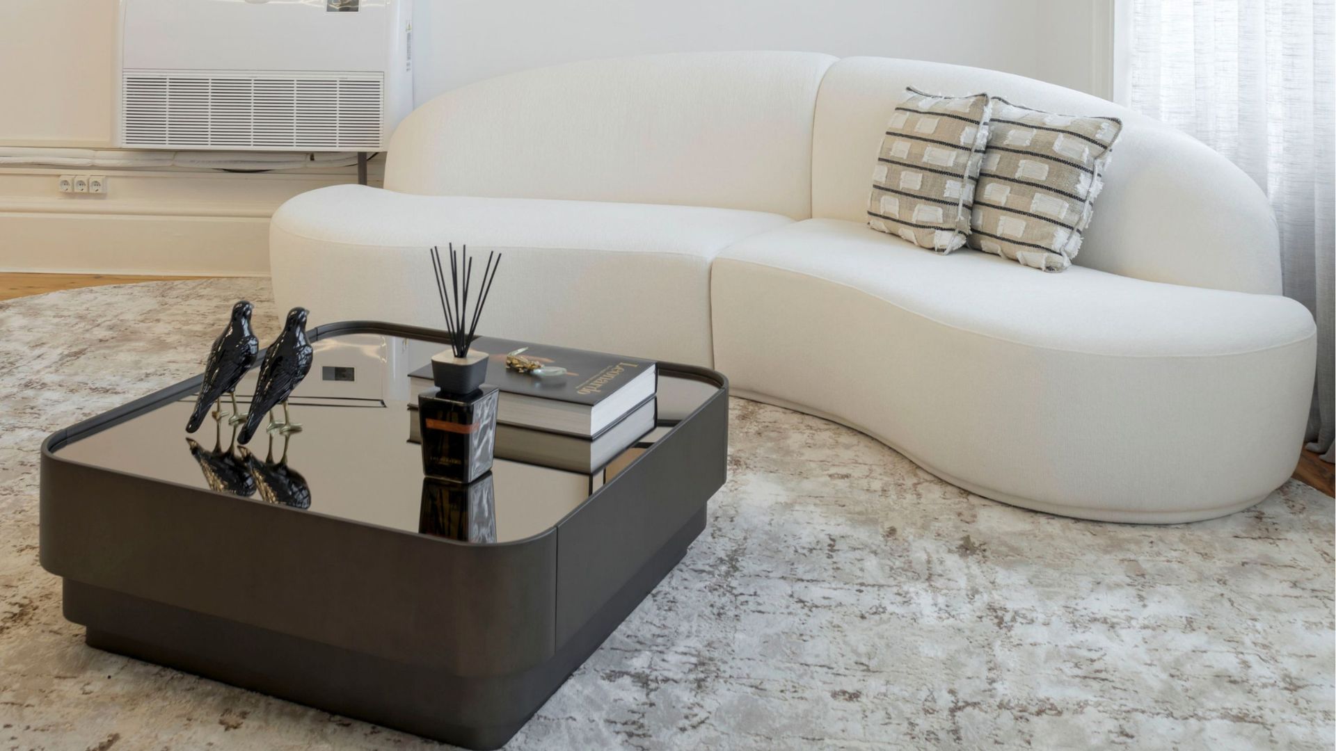 A curved white Cotton Sofa softens the Clérigos Office with its cloud‑inspired silhouette, becoming a sculptural anchor within the luxury living room furniture setting. Paired with a sleek wood coffee table and minimal styling, the scene highlights contemporary living room furniture and the quiet sophistication of custom furniture crafted for modern interiors.