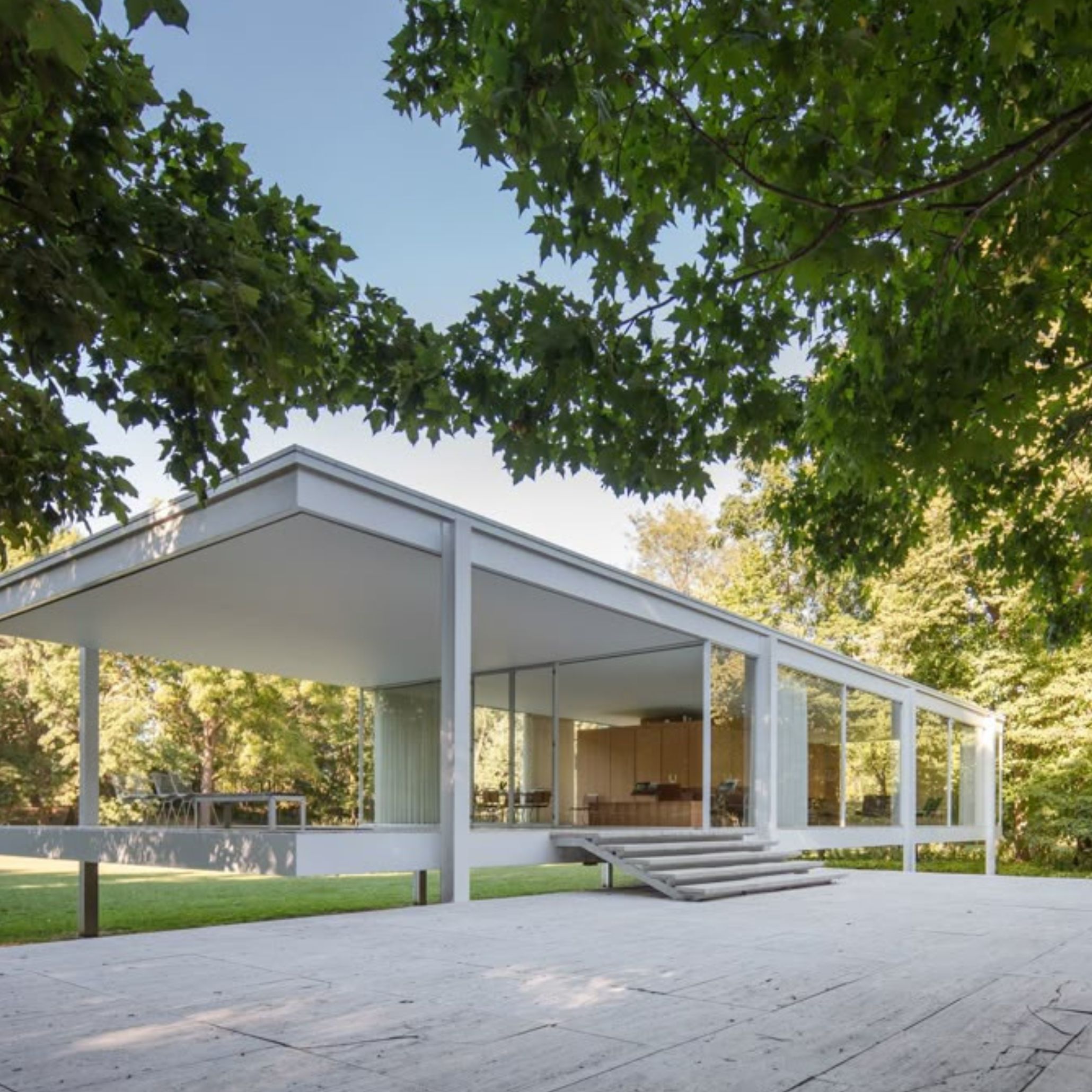 The Farnsworth House rises lightly above the lawn, its exposed steel frame and transparent glass expressing Mies van der Rohe’s belief in structural honesty and spatial freedom. The elevated platform reinforces the principle Less is More, allowing nature, light, and weather to shape the experience of the interior. Through the open façade, the refined design details and custom furniture philosophy behind the project become visible, reflecting a quiet luxury furniture sensibility that continues to influence modern architecture.
