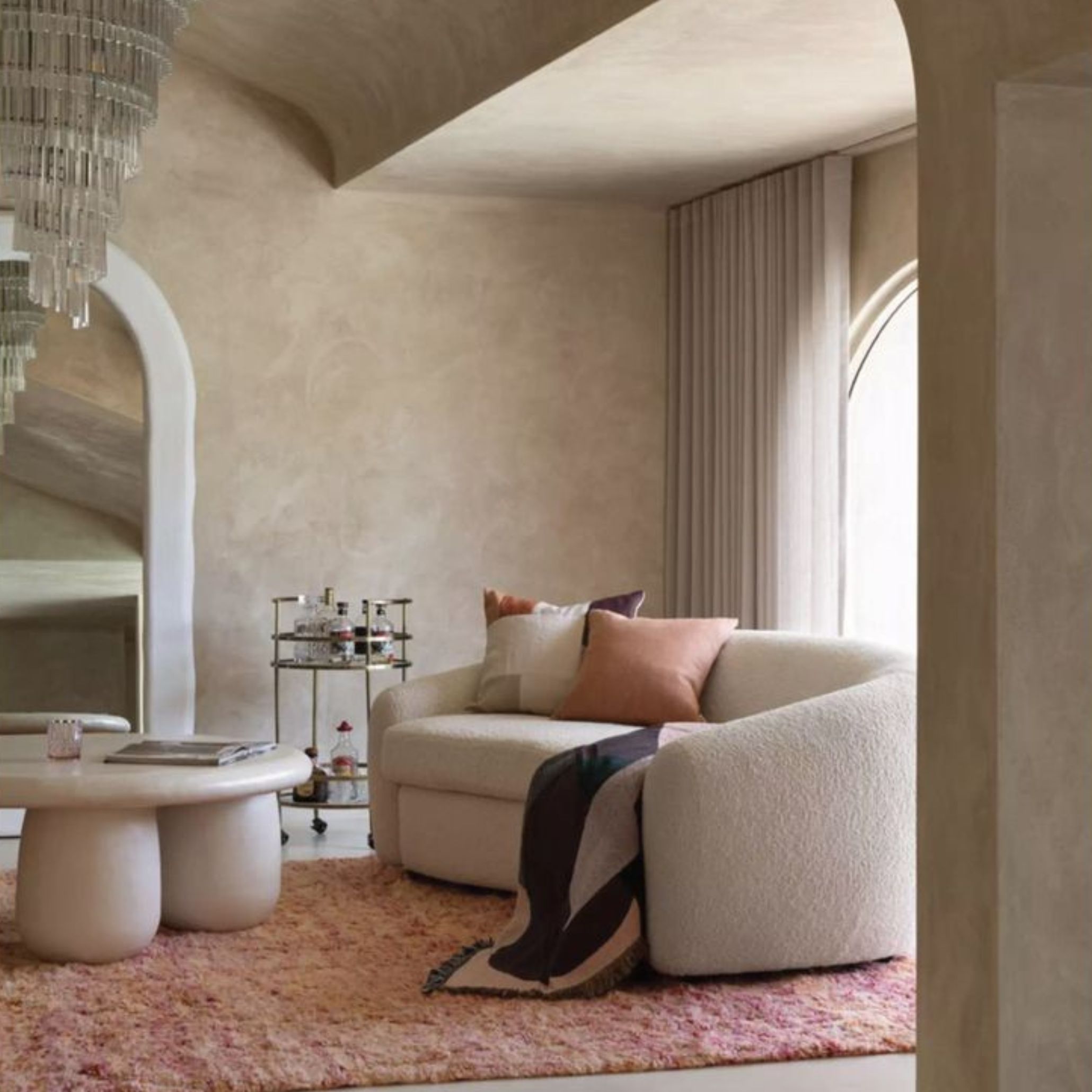 A softly textured living room featuring a curved sofa, a rounded coffee table, and layered textiles that create a warm, sensory atmosphere, complemented by luxury home furniture accents.