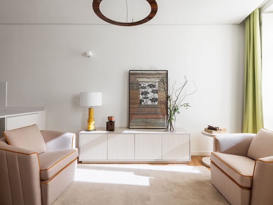 A welcoming living room arranged around two Fortune Armchairs, their soft curves inviting conversation and ease. The Club Side Table adds subtle functionality between seating, while the bespoke Ryan TV Cabinet anchors the wall with its crafted presence. Natural light softens the textures and warm tones, expressing luxury living room furniture, refined interior design inspiration, and the quiet sophistication of a space shaped for hosting.