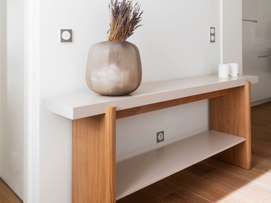 A serene living room vignette centered on the Natur Console, its vertical rhythm and soft natural finish bringing an organic elegance to the space. Styled with a sculptural lamp, framed artwork, and delicate branches, the console’s optional lower shelf enhances its quiet functionality. Light moves gently across its surfaces, expressing luxury living room furniture and the understated sophistication that defines the hosting area.