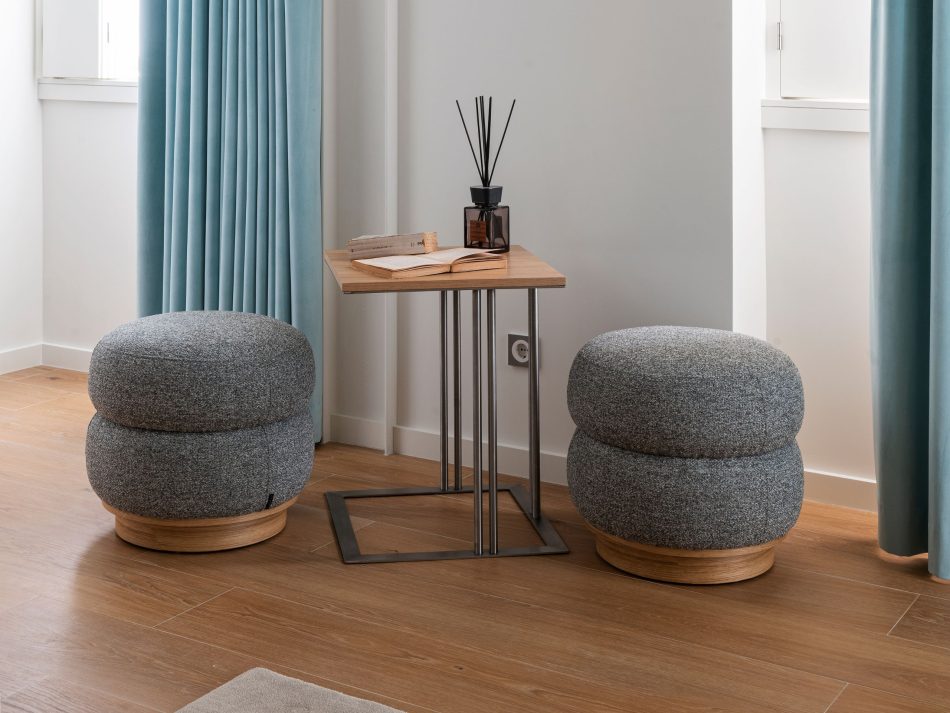 A quiet seating corner where the Louise Side Table sits between two upholstered stools, its clean lines and warm wood presence adding a functional, intimate accent to the living room. Soft light, gentle textures, and a calm palette shape an atmosphere of modern furniture, understated living room design, and the welcoming elegance intended for guests.