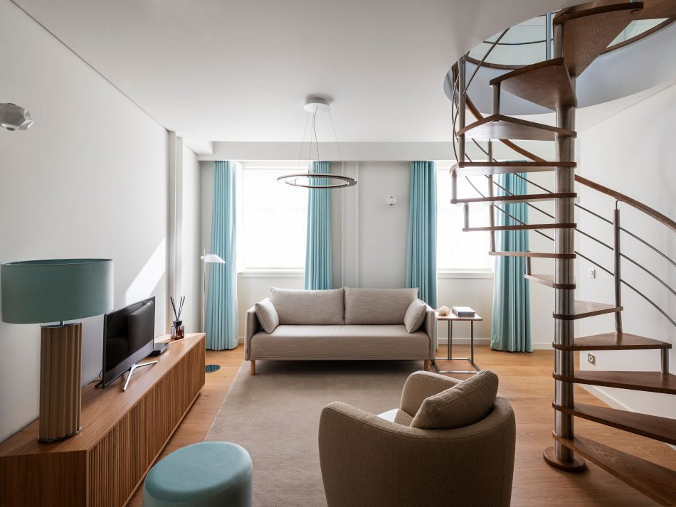 A serene guest living room where the bespoke Ryan TV Cabinet defines the space with quiet structure, complemented by the Her Armchair’s soft, inviting presence. The Louise Side Table and Thomas Stool introduce functional accents that feel intimate and unobtrusive. Natural light softens the materials, creating an atmosphere shaped by luxury living room furniture, warm interior design inspiration, and the understated elegance of a space designed for guests.