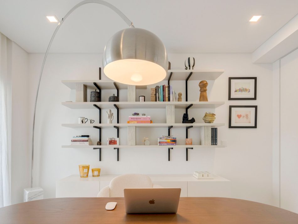 A contemporary workspace centered around a bespoke Natur Dining Table adapted as a refined desk, paired with a soft upholstered chair and illuminated by a sculptural arc lamp. Behind it, the Natur Bookcase displays curated books and decorative objects, creating a sense of rhythm and intentionality. The atmosphere blends the clarity of office furniture with the crafted warmth of bespoke furniture solutions, elevated by subtle touches of luxury home furniture that make the room both functional and inspiring.