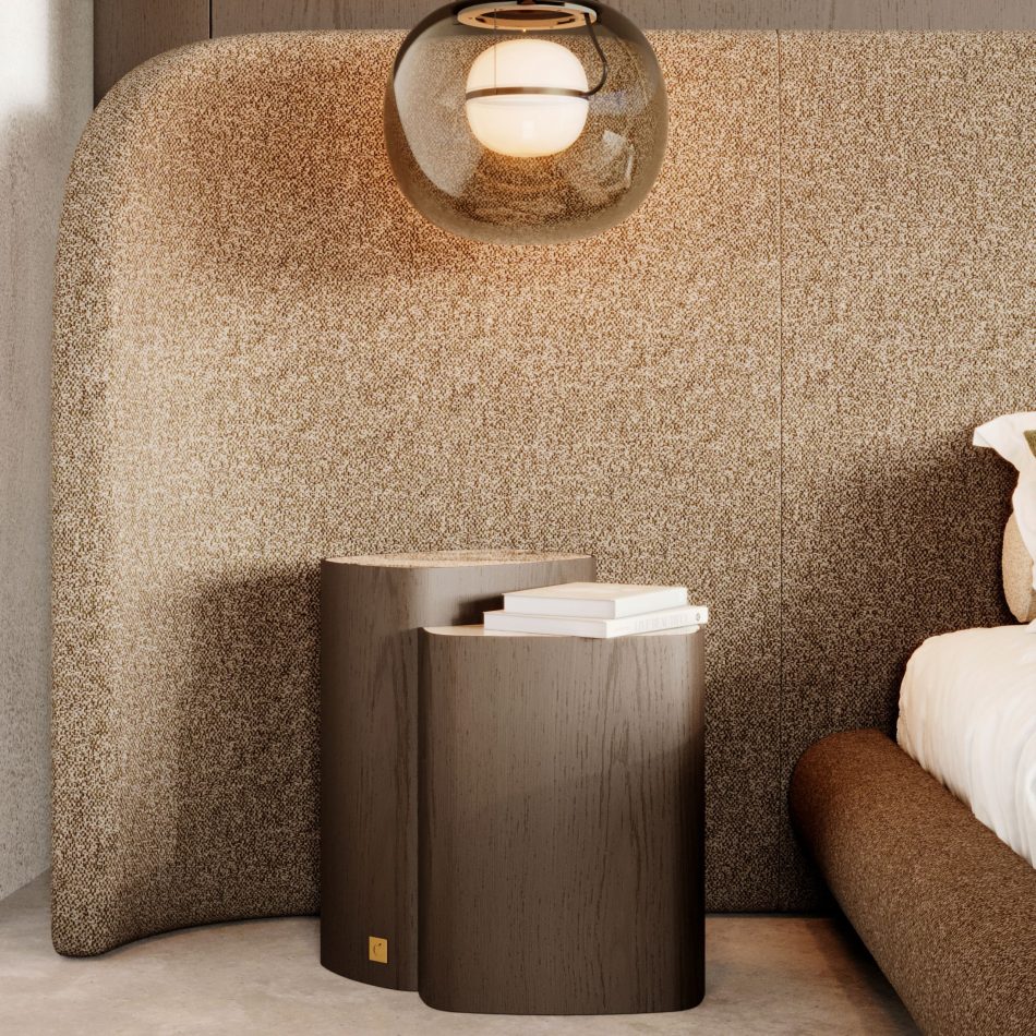 A warm bedroom corner showcases the Dolomites Side Table in its dual‑form silhouette, crafted in dark brown wood with a silver travertine marble top, positioned against a softly curved wall panel and illuminated by a warm pendant light, creating an atmosphere of quiet refinement aligned with luxury furniture, the tactile honesty of high end furniture, and the sculptural clarity of contemporary furniture.