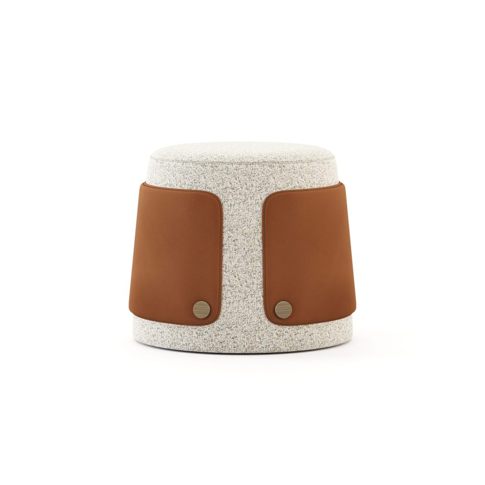 The Dolomites Stool is shown as a softly rounded form wrapped in textured light upholstery, its silhouette tapering gently toward the floor in a way that recalls stone shaped slowly by nature. Two warm brown leather panels frame the sides with intention, each secured by round brass buttons that emphasize the crafted detailing found in luxury furniture and contemporary custom furniture. The combination of soft curves and contrasting materials creates a calm, grounded presence that feels both organic and refined.