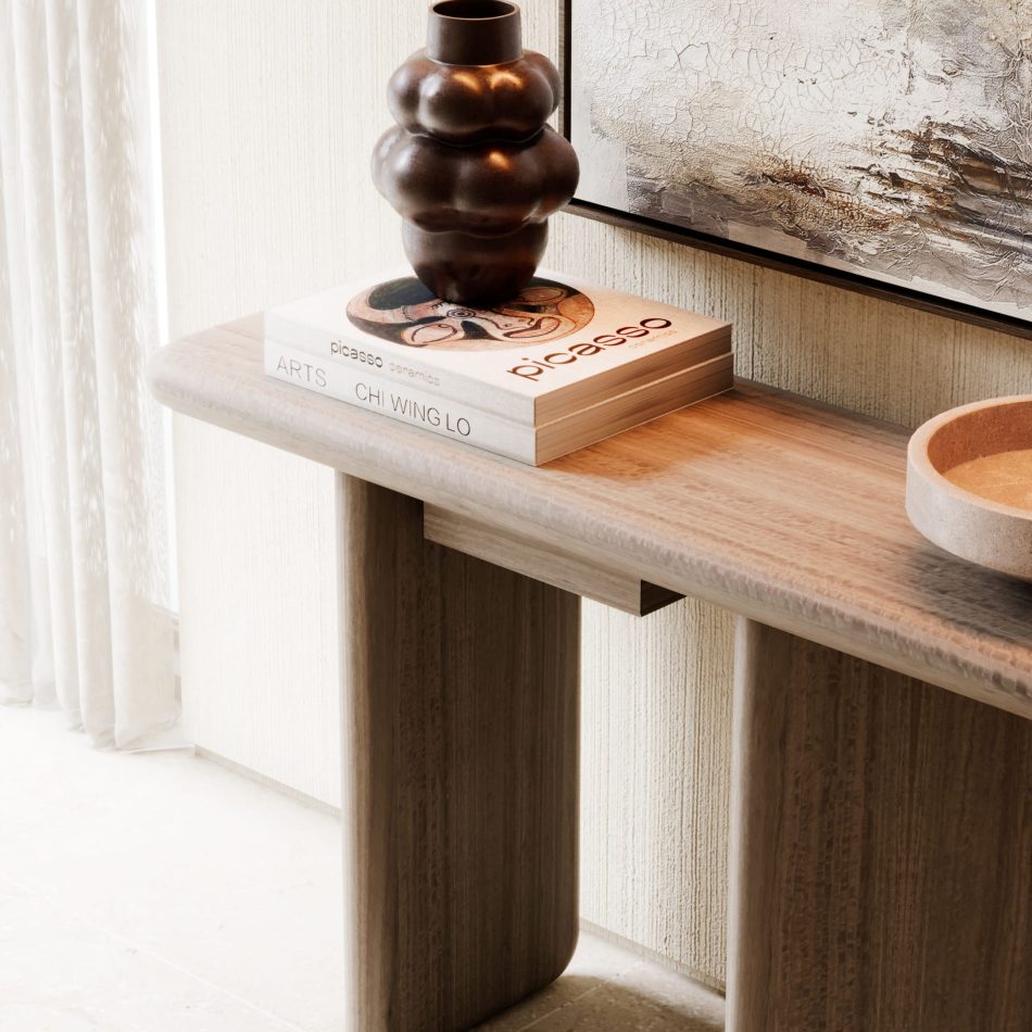Close‑up of the Foz Console highlights the sculptural arrangement of a dark vase resting on two art books. The rounded wood edge of the console introduces warmth and material depth. The styling reflects the quiet refinement associated with luxury home furniture. Soft natural light and layered textures contribute to a calm, modern living room design. The composition offers subtle interior design inspiration through its balance of art, furniture, and tone.