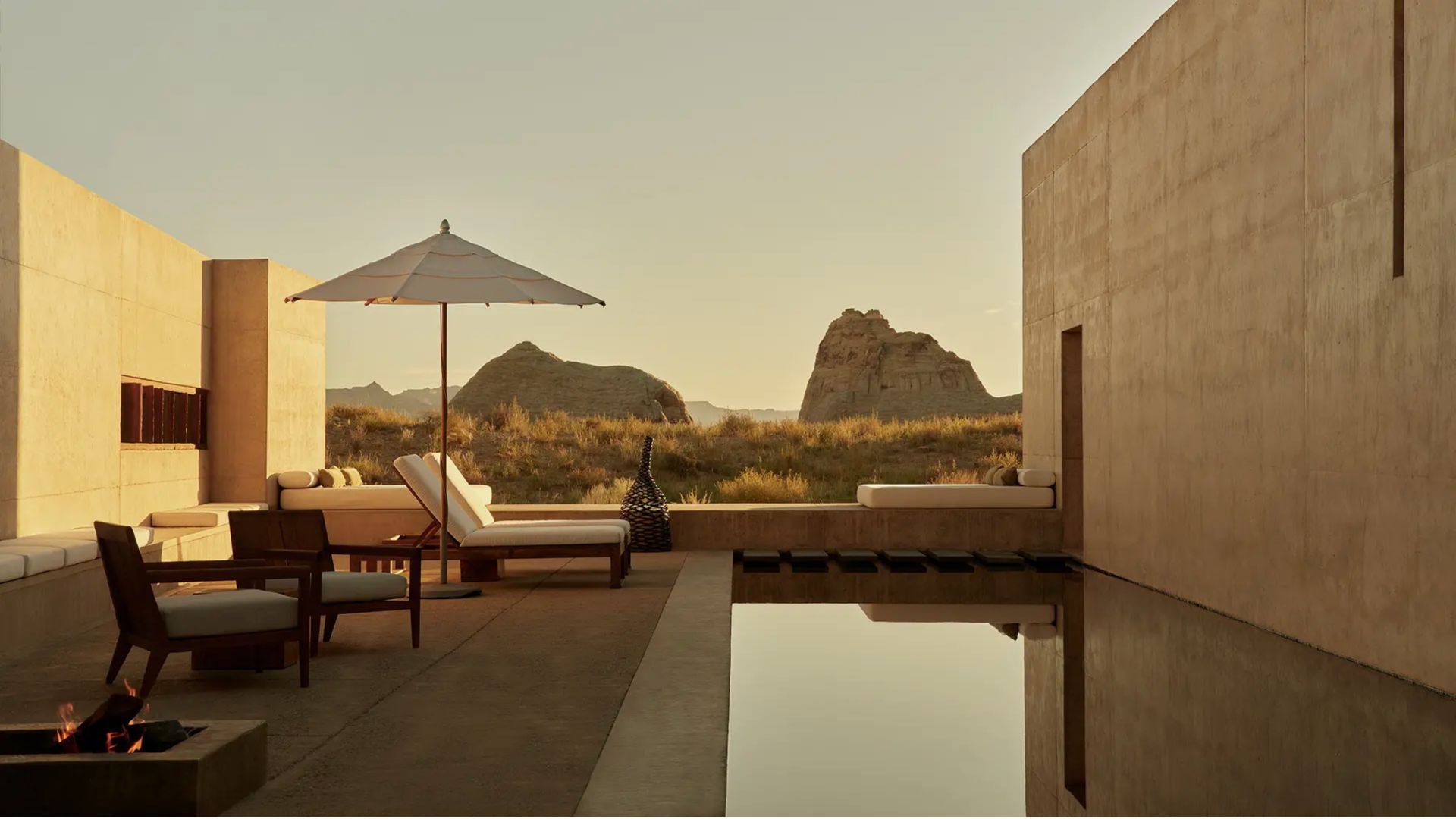 A peaceful desert wellness lounge featuring minimalist seating, a reflecting pool, and shaded areas that echo Indigenous traditions of rest and contemplation. The clean architectural lines blend with the rocky landscape, creating a serene retreat enhanced by subtle luxury home furniture, earthy modern furniture elements, and the grounding presence of solid wood accents that support mindful interaction with nature.