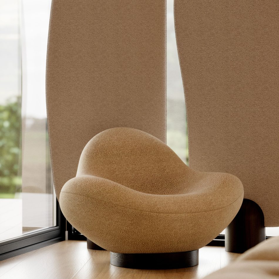 A warm interior setting frames the Stone Armchair, upholstered in light brown textured fabric and positioned near large windows with a curved vertical screen, where natural daylight enhances its smooth, rounded contours and wood base, creating an atmosphere of quiet luxury rooted in high end furniture, earthy home furniture, and modern living room design.
