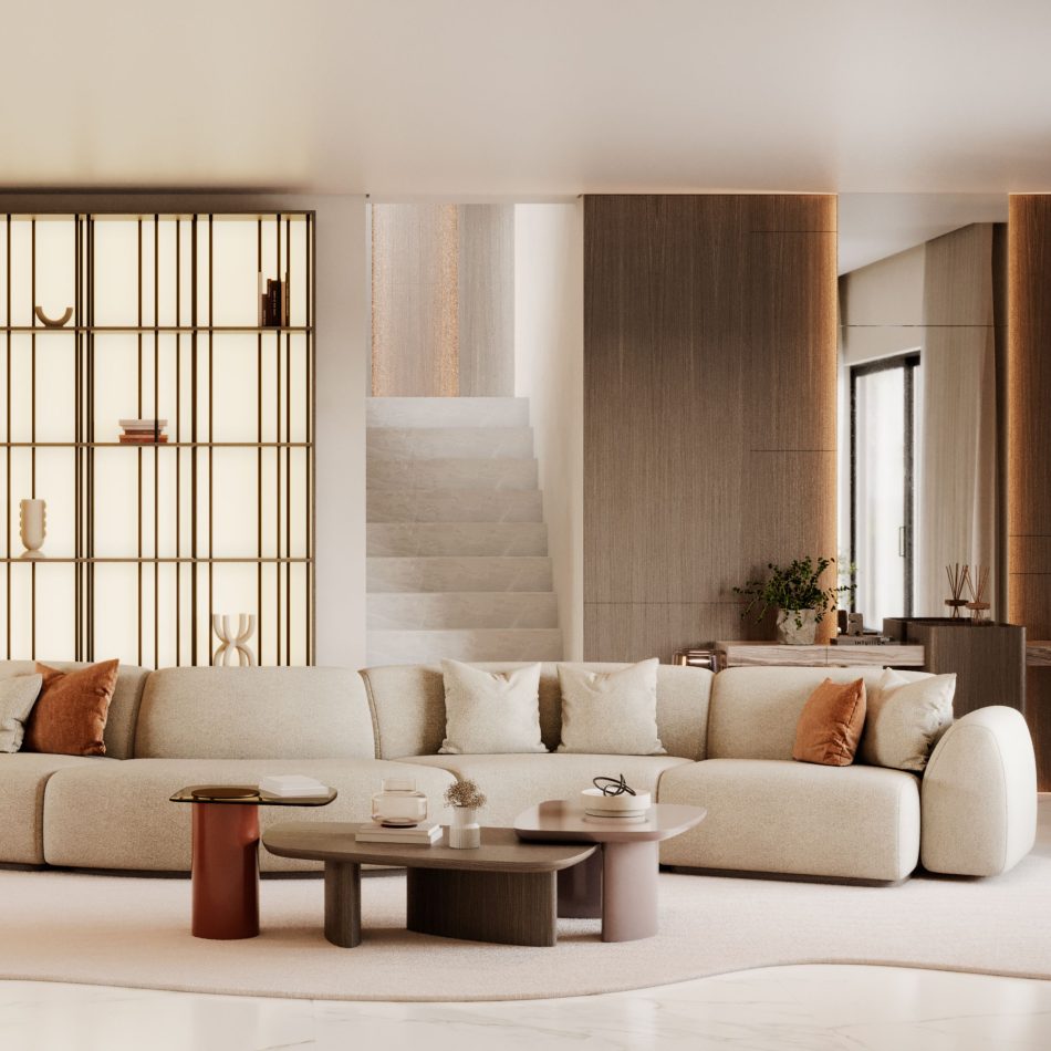 The Stone Sofa in a spacious modern living room, upholstered in light neutral tones and layered with plush beige and rust pillows, positioned before rounded contemporary tables and framed by softly lit shelving, creating a serene atmosphere shaped by curated living room furniture, subtle hints of bespoke furniture, refined touches of modern furniture, and the calm elegance associated with elevated interior design inspiration.