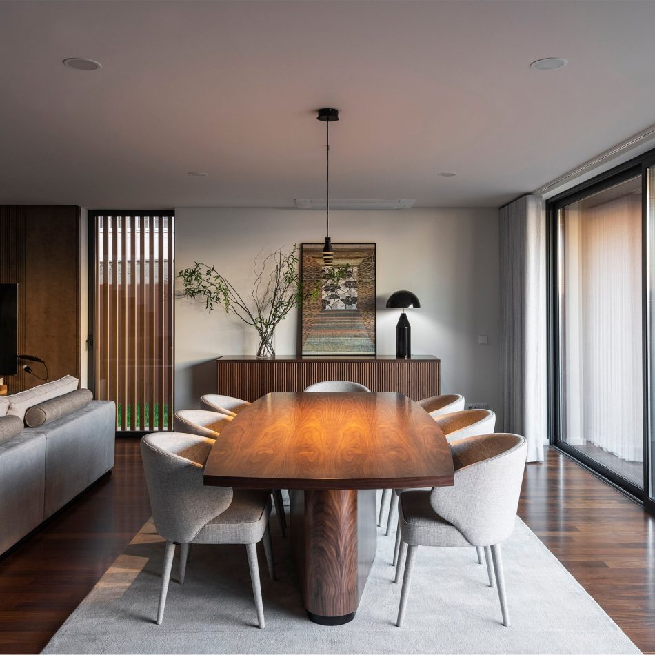 A elegant dining room defined by the Elea Dining Table in rich walnut, surrounded by Fortune Chairs whose clean lines and natural textures bring warmth to the composition. Behind them, the Manhattan Sideboard introduces structure through its crafted detailing, adding depth and permanence to the space. Soft natural light enhances the material richness, creating an atmosphere shaped by luxury dining room furniture, bespoke furniture, and the calm balance of contemporary furniture.
